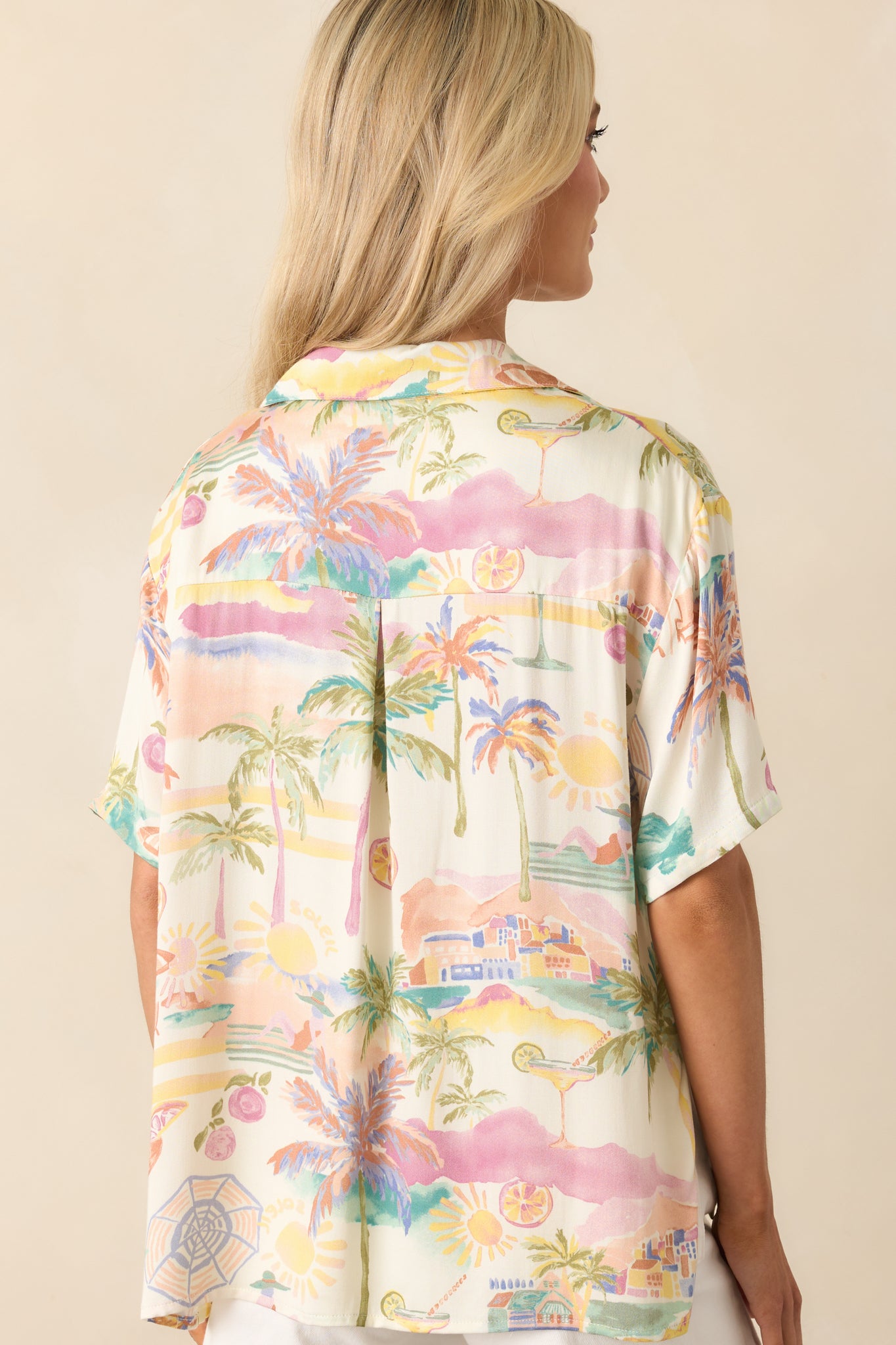 A view from behind of the ivory tropical print top, displaying the short sleeves, relaxed fit, and slight hi-low hem.