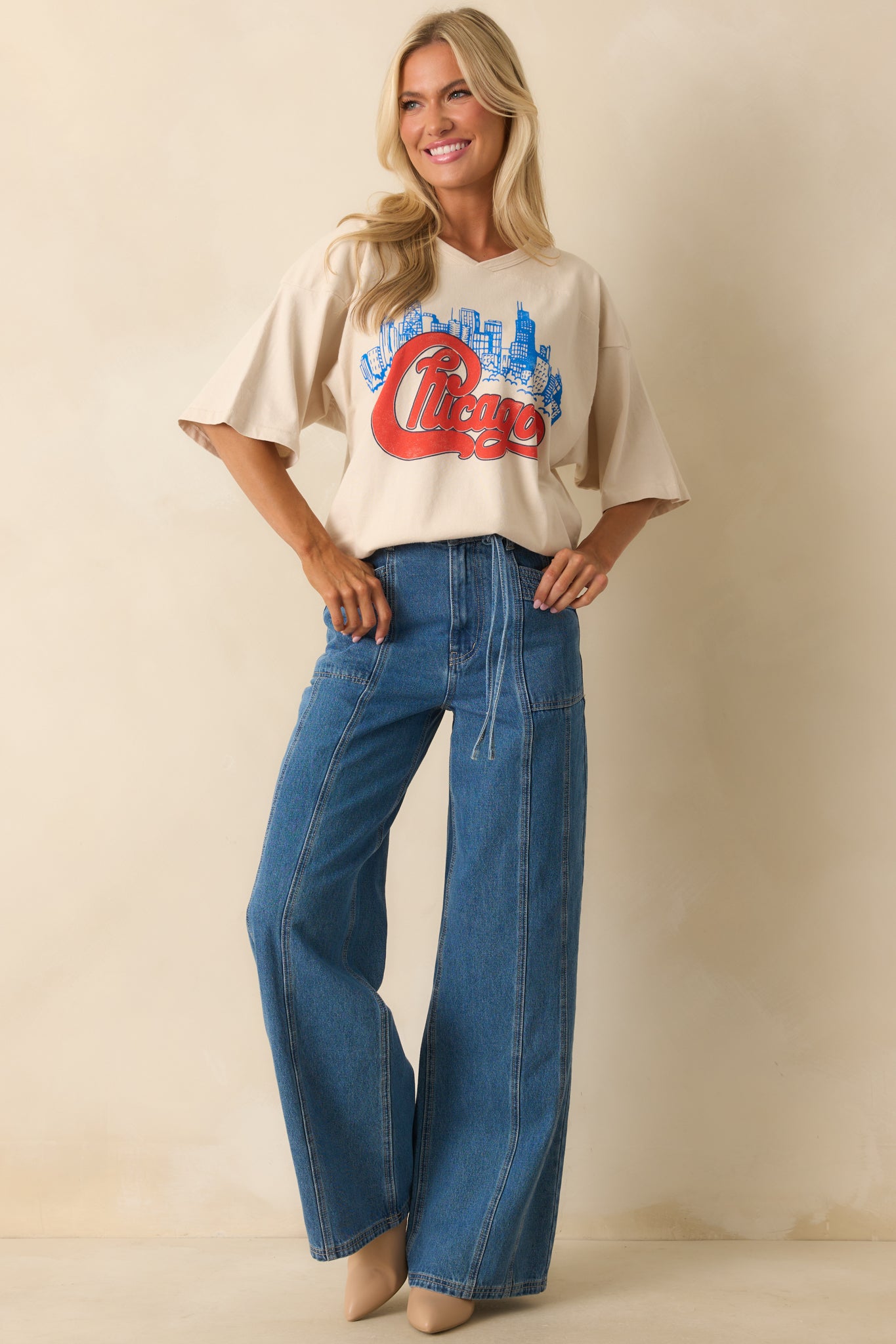 Ivory oversized T-shirt front design showcasing vibrant “Chicago” script atop blue skyline print, paired with casual dropped-shoulder silhouette.