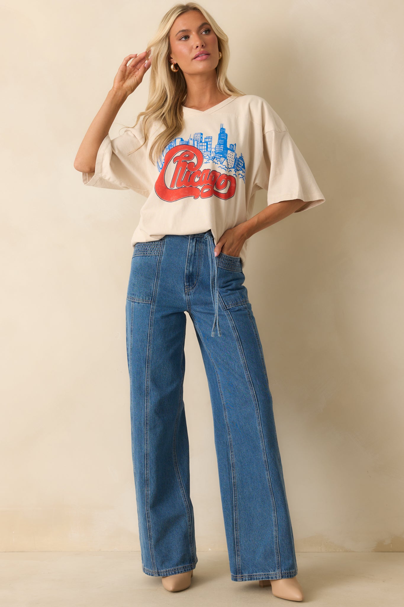 Entire ivory oversized T-shirt displaying graphic blend of red “Chicago” text and vivid blue skyline, designed with v-stitch collar and loose sleeves.