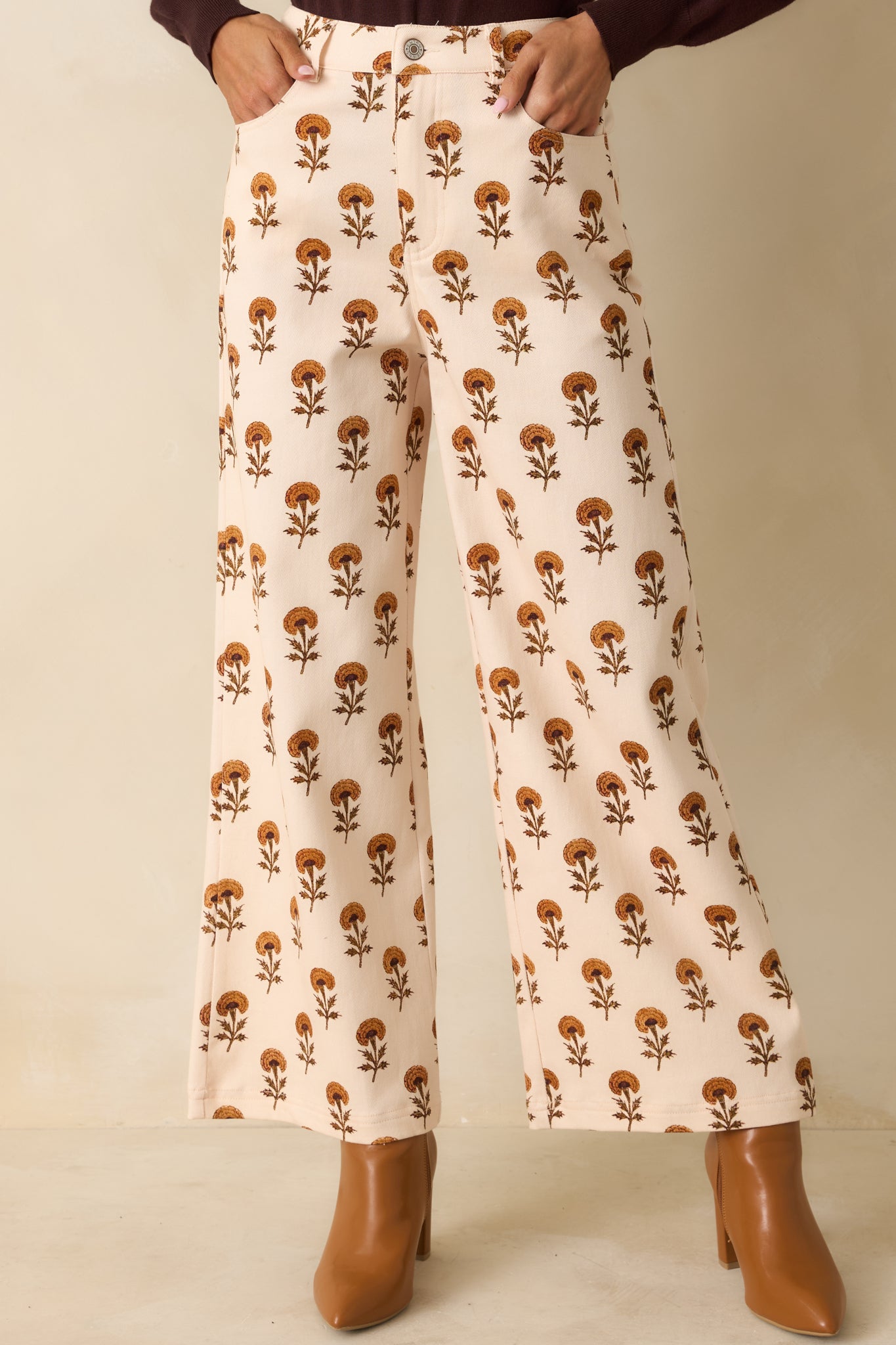 Ivory wide leg pants with high-rise waist, marigold floral print, front button and zip closure, and side pockets.