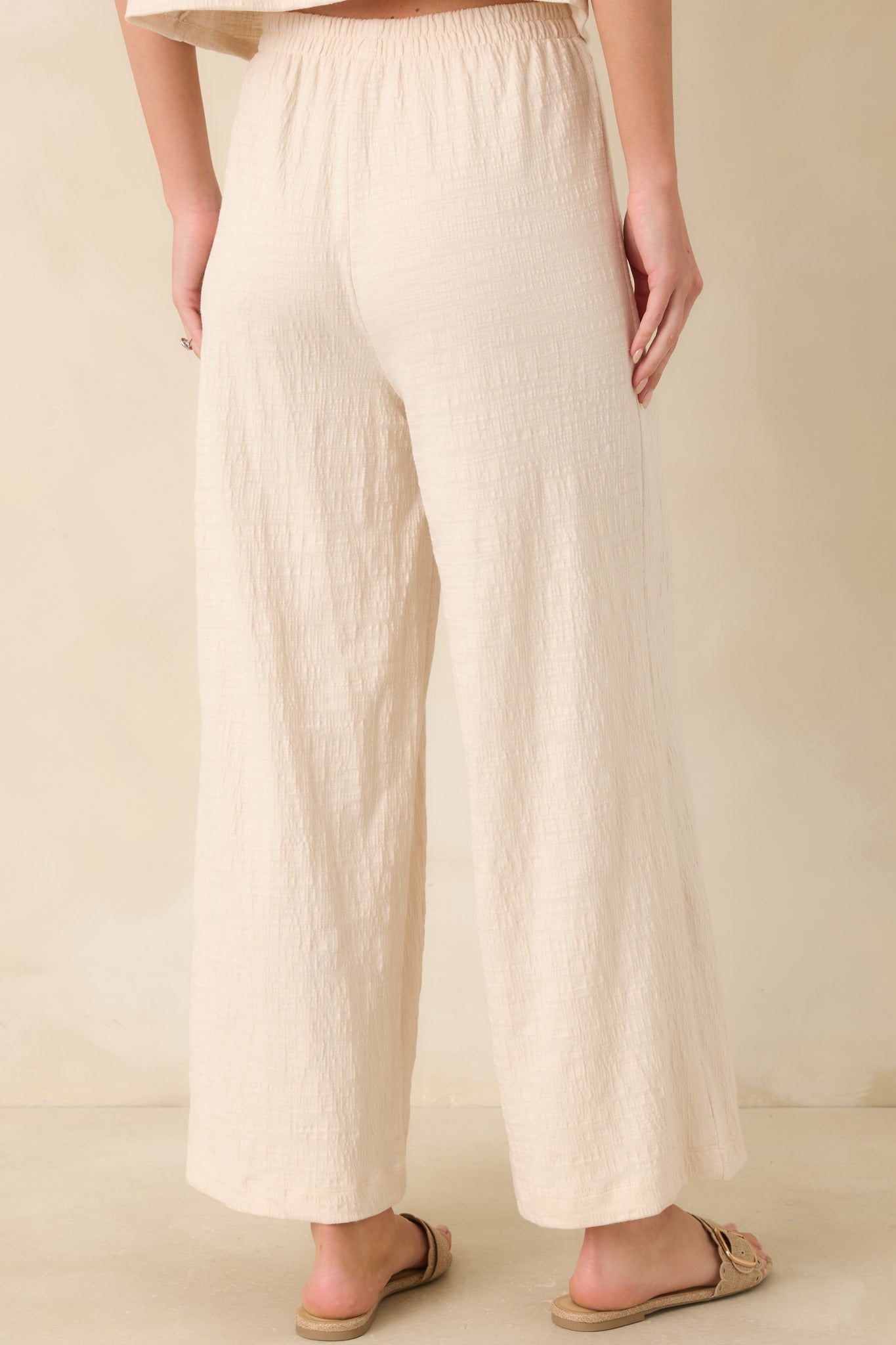 Ivory wide-leg pants with elastic waistband and relaxed rear drape.