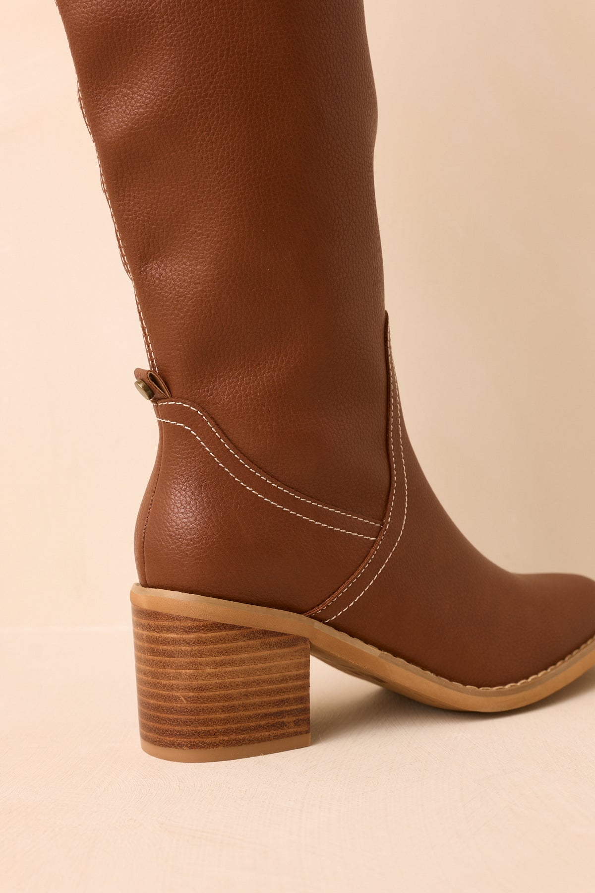 Rear of the knee-high faux leather boots shows the tall shafts, curved stitching, and stacked block heels.