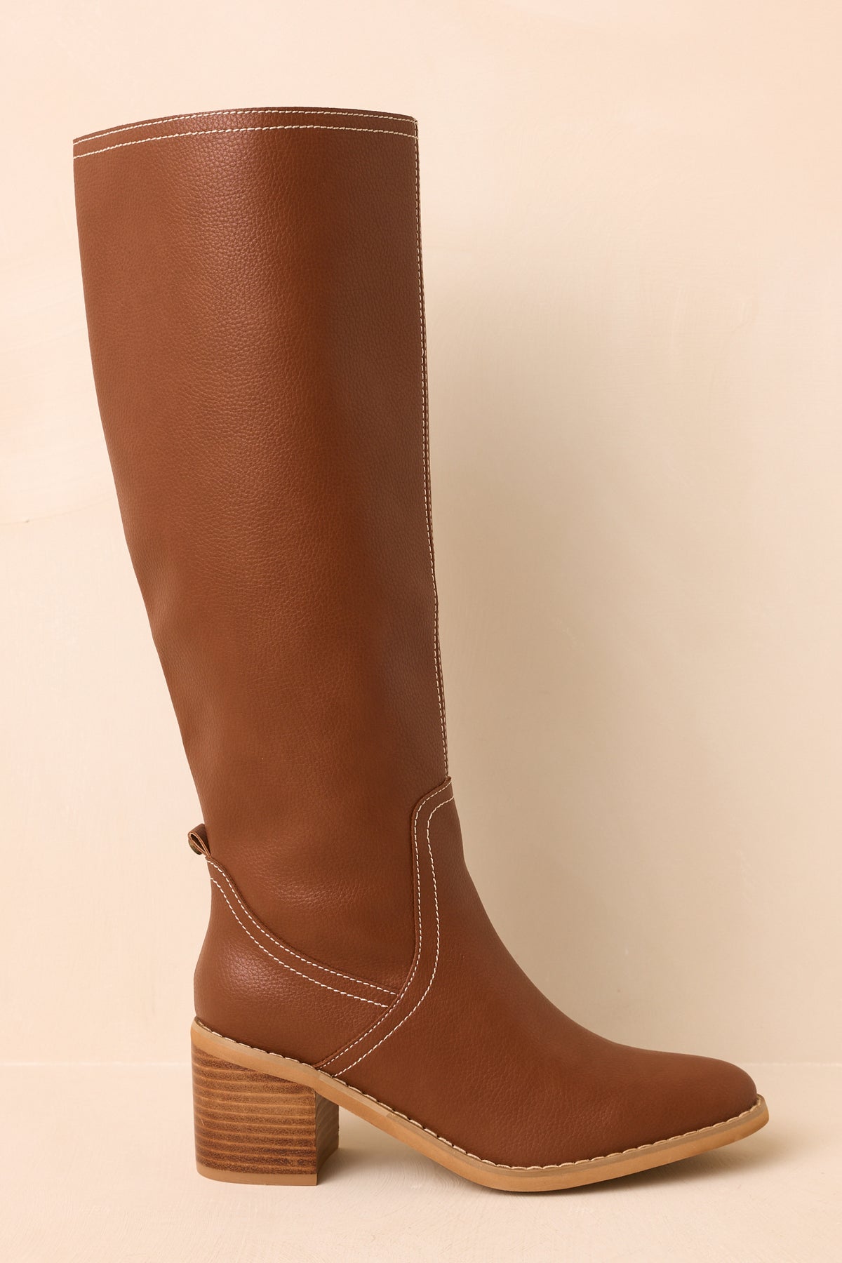Knee-high faux leather boots display their streamlined shaft and stacked block heel from a side angle.