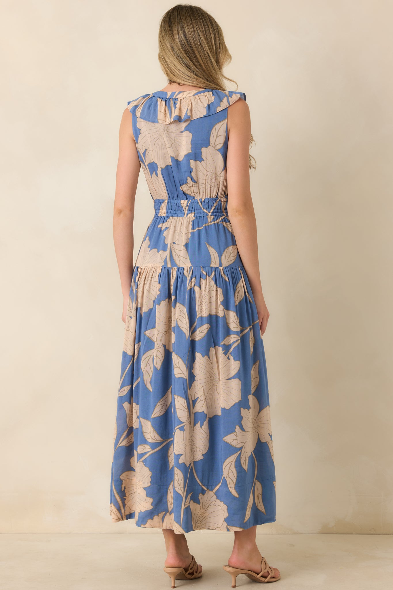 Lake blue floral maxi dress showing the back of the sleeveless silhouette with a smocked waistband and flowing tiered skirt.