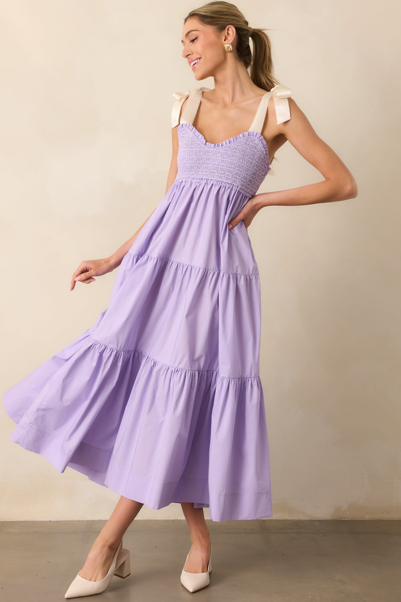 A dreamy lavender midi dress with ivory self-tie bow straps, intricate white embroidery, and a flattering smocked bodice.