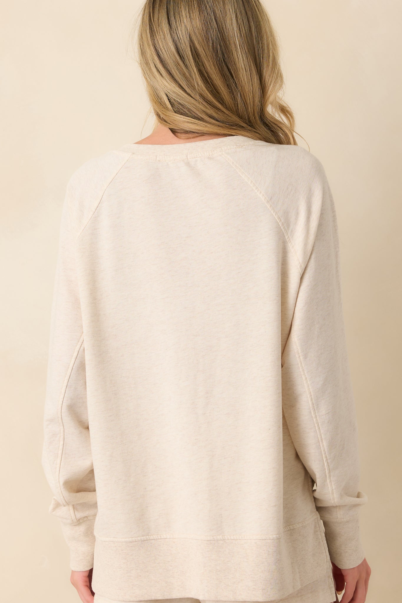 A view from behind of the light beige sweatshirt displaying its relaxed shape and the subtle flow of the lightweight fabric.