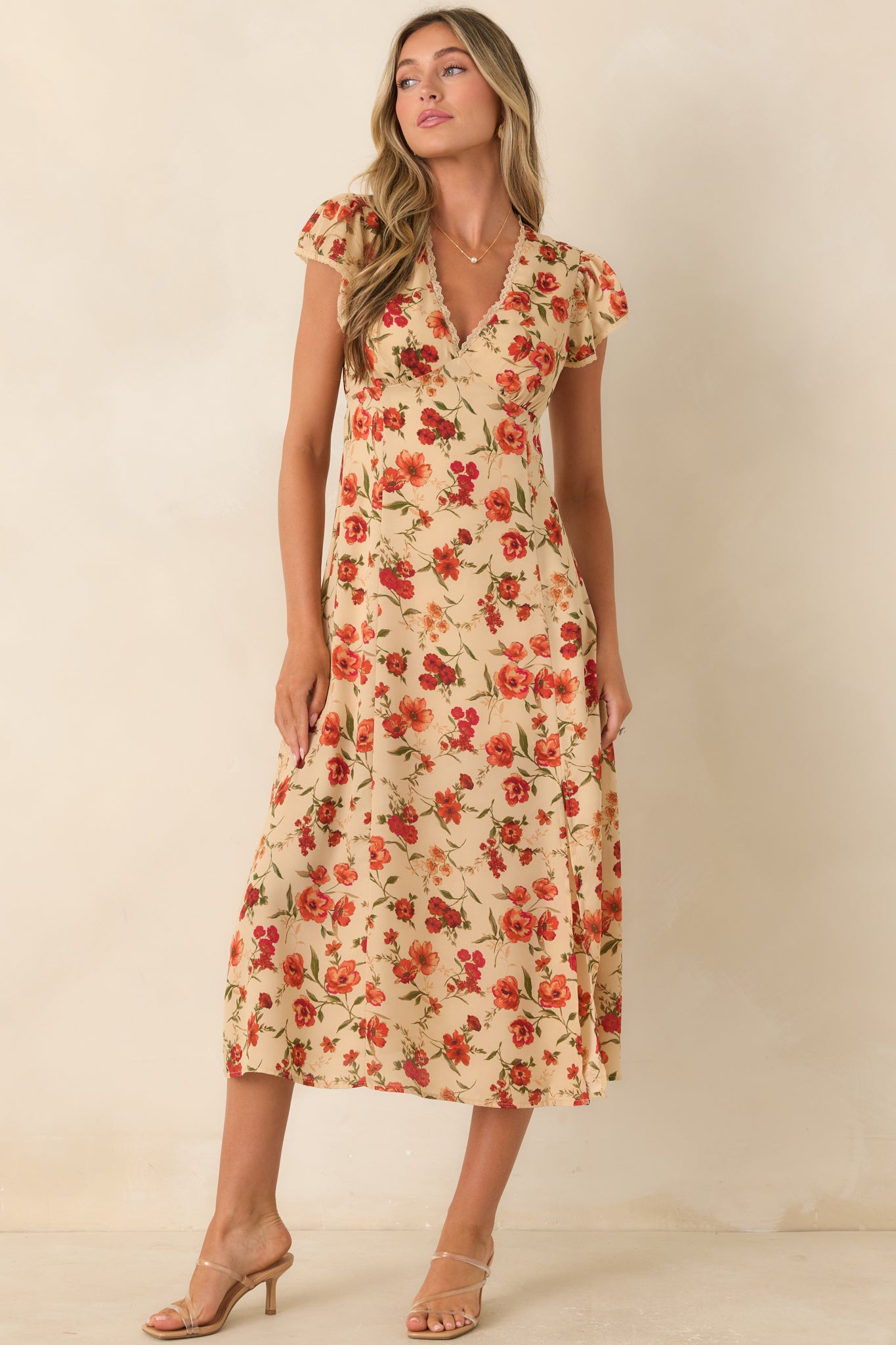 Light beige floral midi dress featuring a surplice lace-trimmed V-neckline, flutter sleeves, an empire waist, adjustable back tie, and a flowing skirt with a side slit.