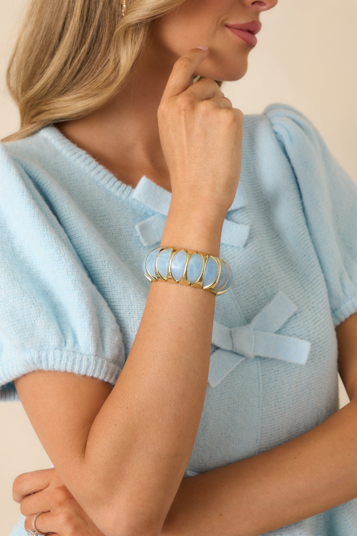 Cropped view of the light blue and gold stretch bracelet featuring sculptural blue beads held within polished gold-tone links.