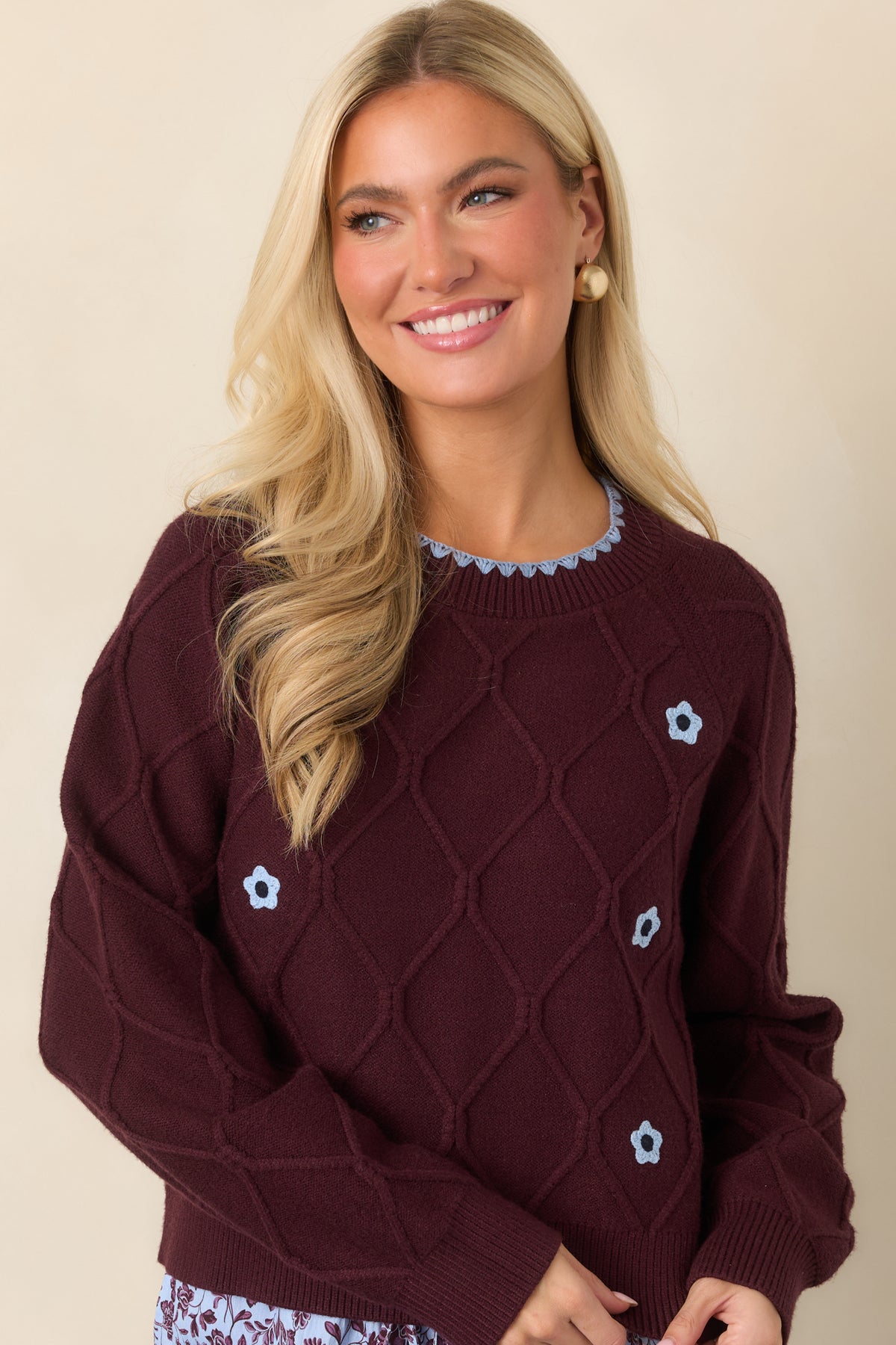 Light blue floral accents line both sides of the sweater’s textured front beneath a scalloped crew neckline.