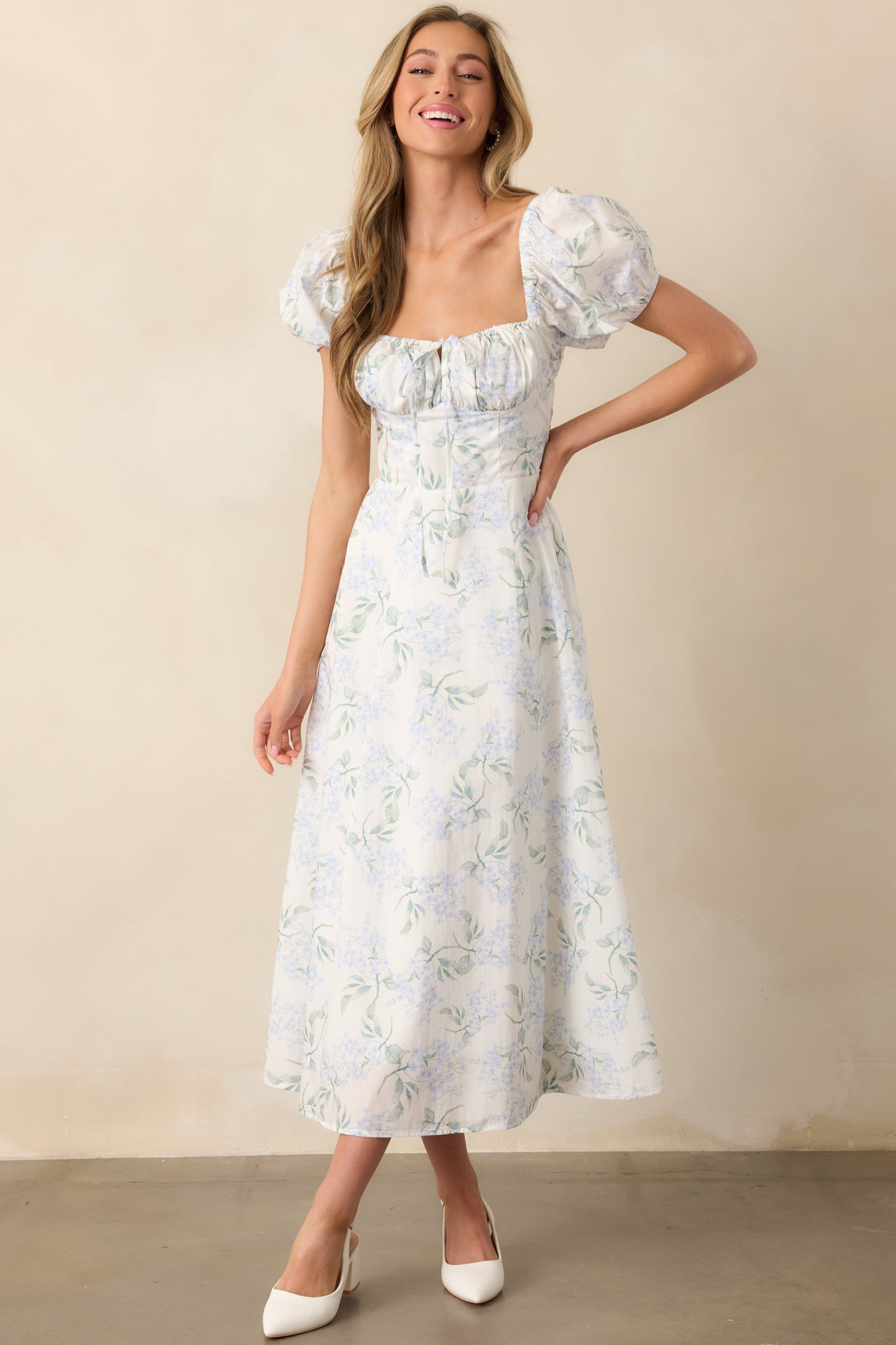 A full-body front view of a light blue floral print maxi dress, featuring an elastic adjustable sweetheart neckline, bustier-style stitching throughout the bodice, and short puff sleeves with elastic cuffs.