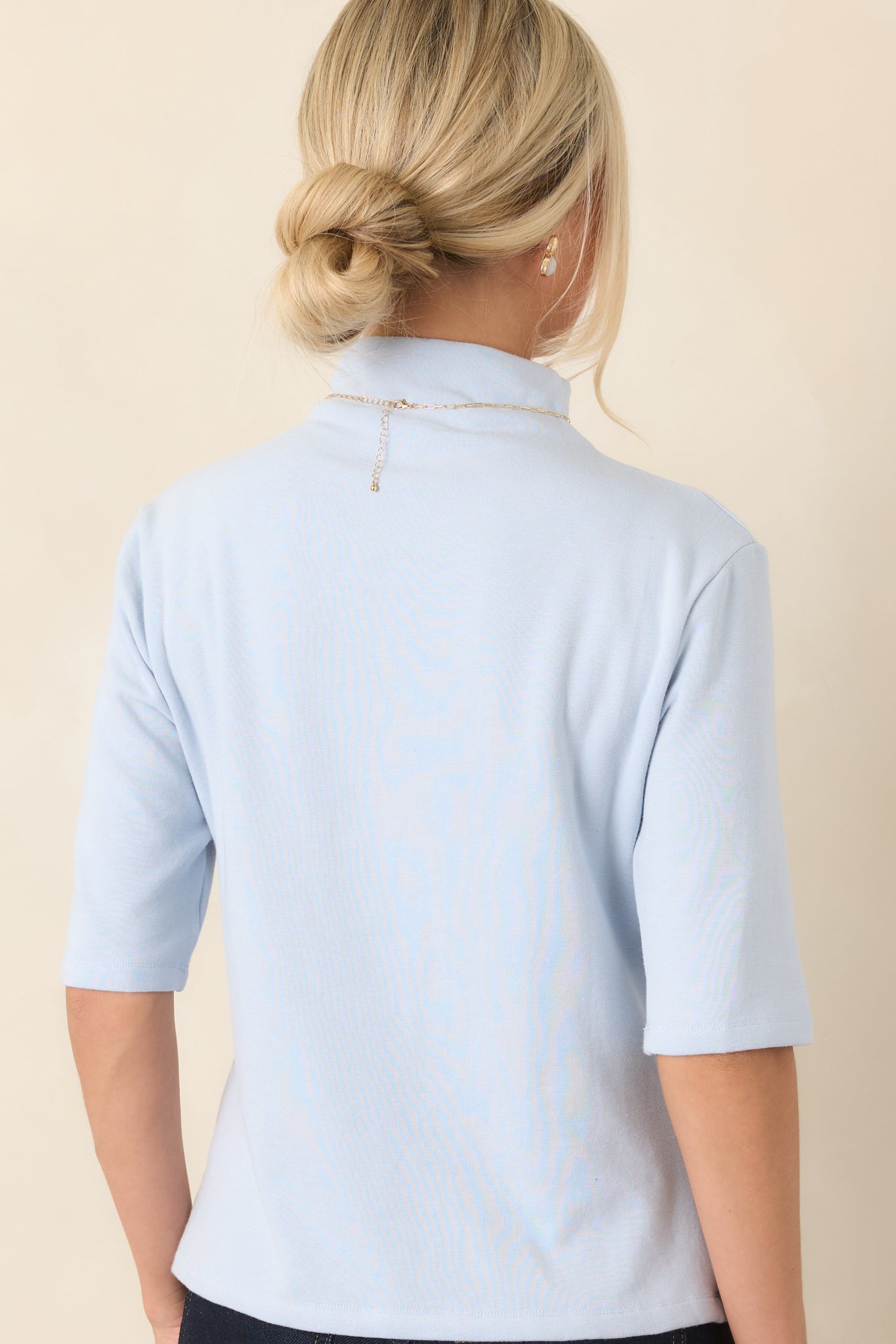 Rear view of the light blue knit top highlighting its smooth knit construction, gently fitted shape, and elbow-length sleeves.
