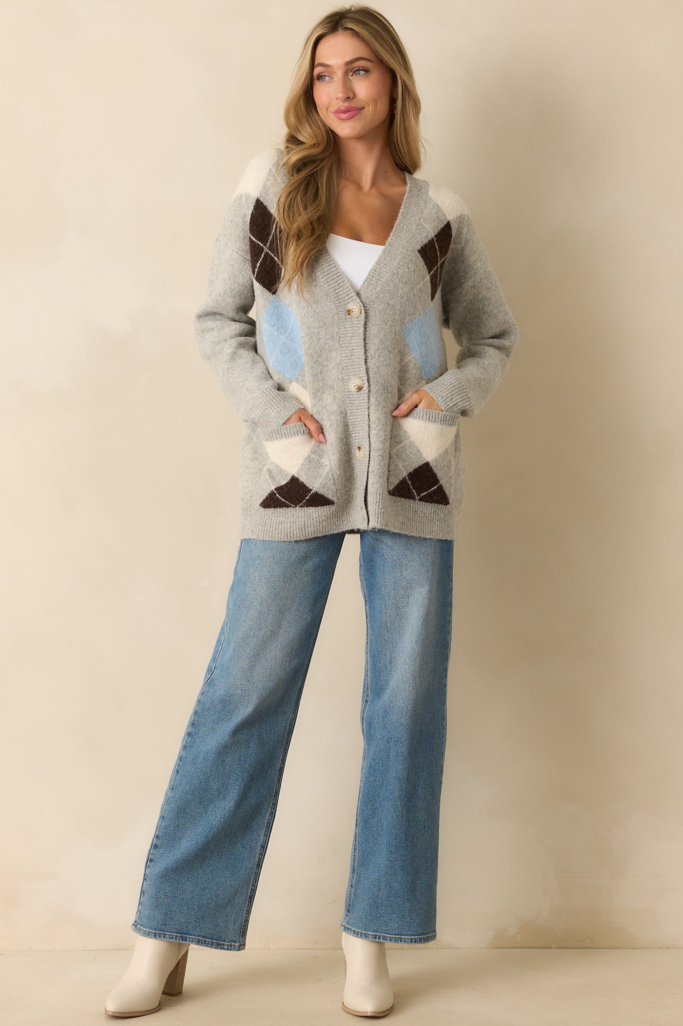 A front view of the light grey cardigan featuring an ivory, brown, and blue argyle pattern across the front and a deep v-neckline.