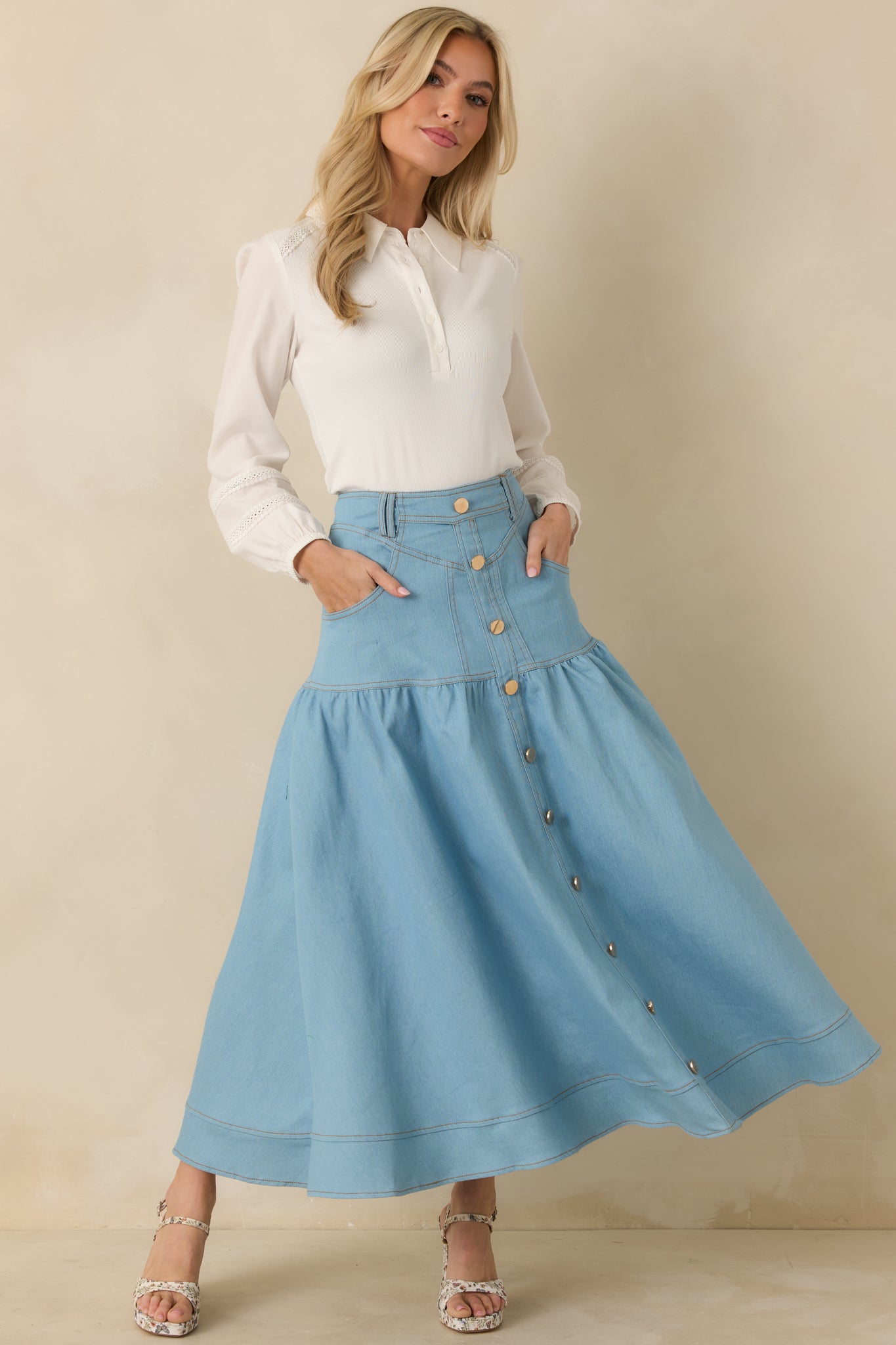 Light wash denim maxi skirt with high-rise waistband, gold-tone button-down front, and tiered flared silhouette.
