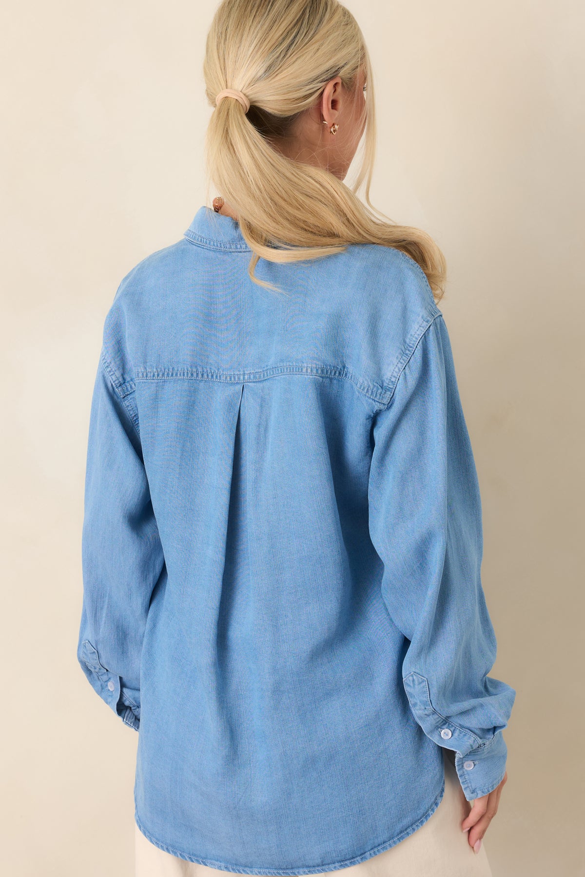 Rear view of the lightweight denim top showcasing its relaxed drape, subtle fading, curved high-low hem, and smooth back panel.
