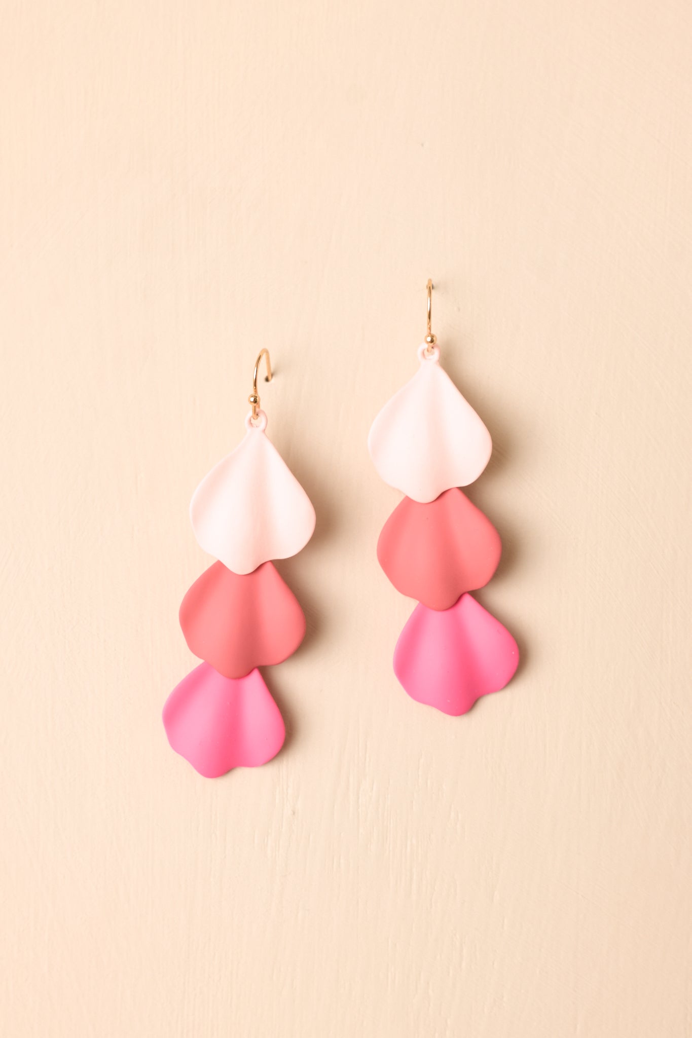 Pair of lightweight earrings displayed against a beige background highlighting the fluid petal shape.