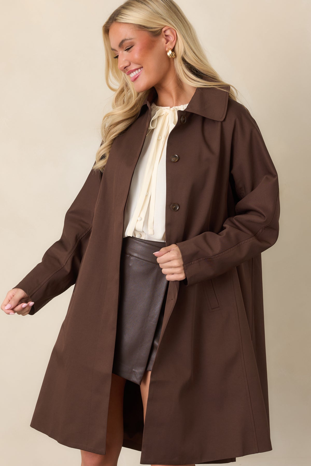 Long chocolate coat highlighting its smooth fabric and relaxed proportions.