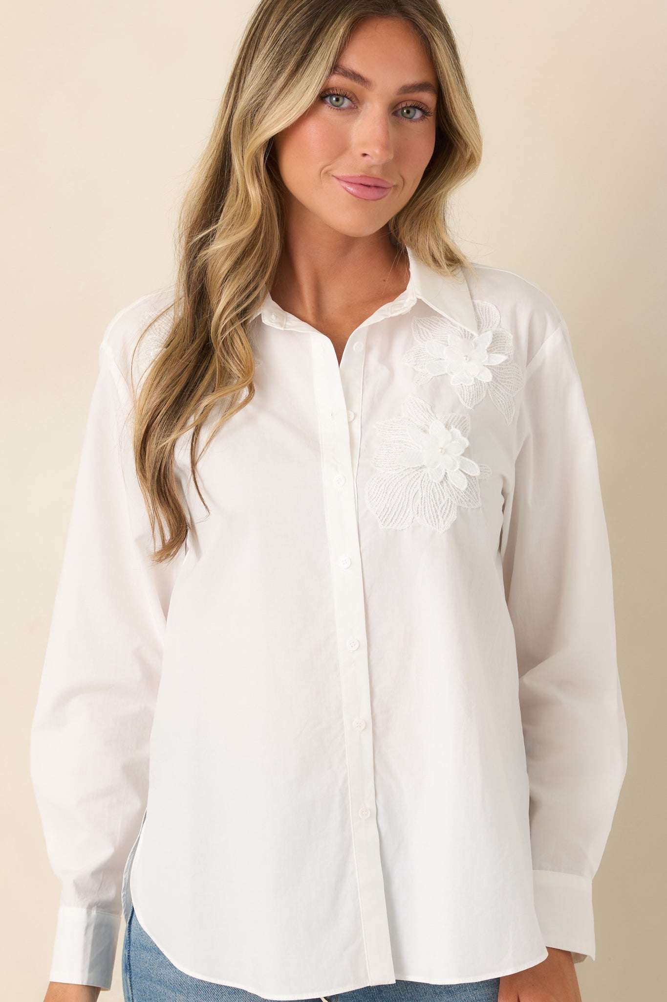 Front detail of the blouse featuring long sleeve cuffs, floral appliqué accents, and polished tailoring.