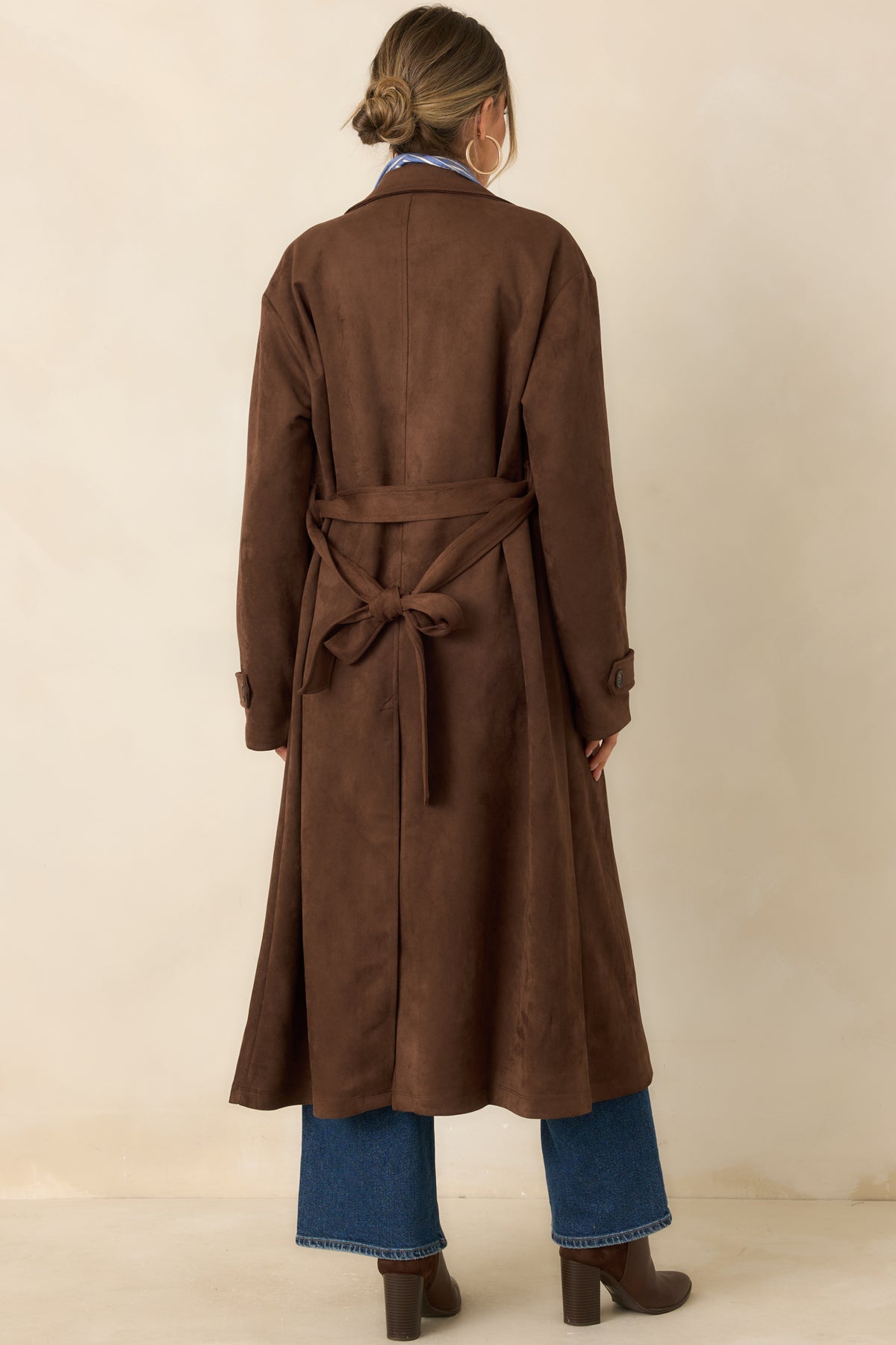 Rear view of the longline coat showcases its smooth tailored back, matching waist belt, and long sleeves with buttoned cuff tabs.