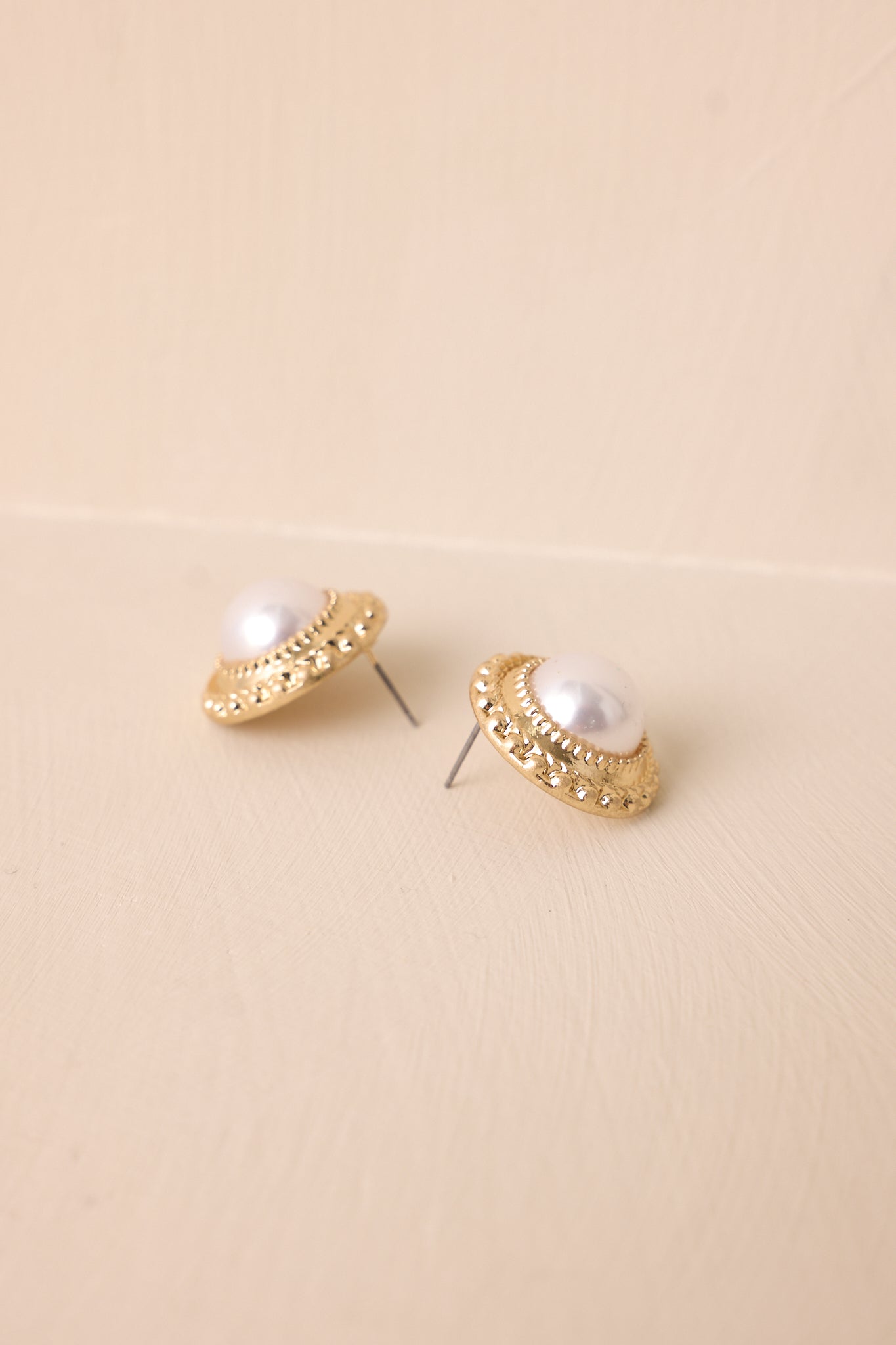 A zoomed-in look at the earrings, highlighting the intricate gold borders and the smooth, lustrous ivory pearl in the center of the large circular design.
