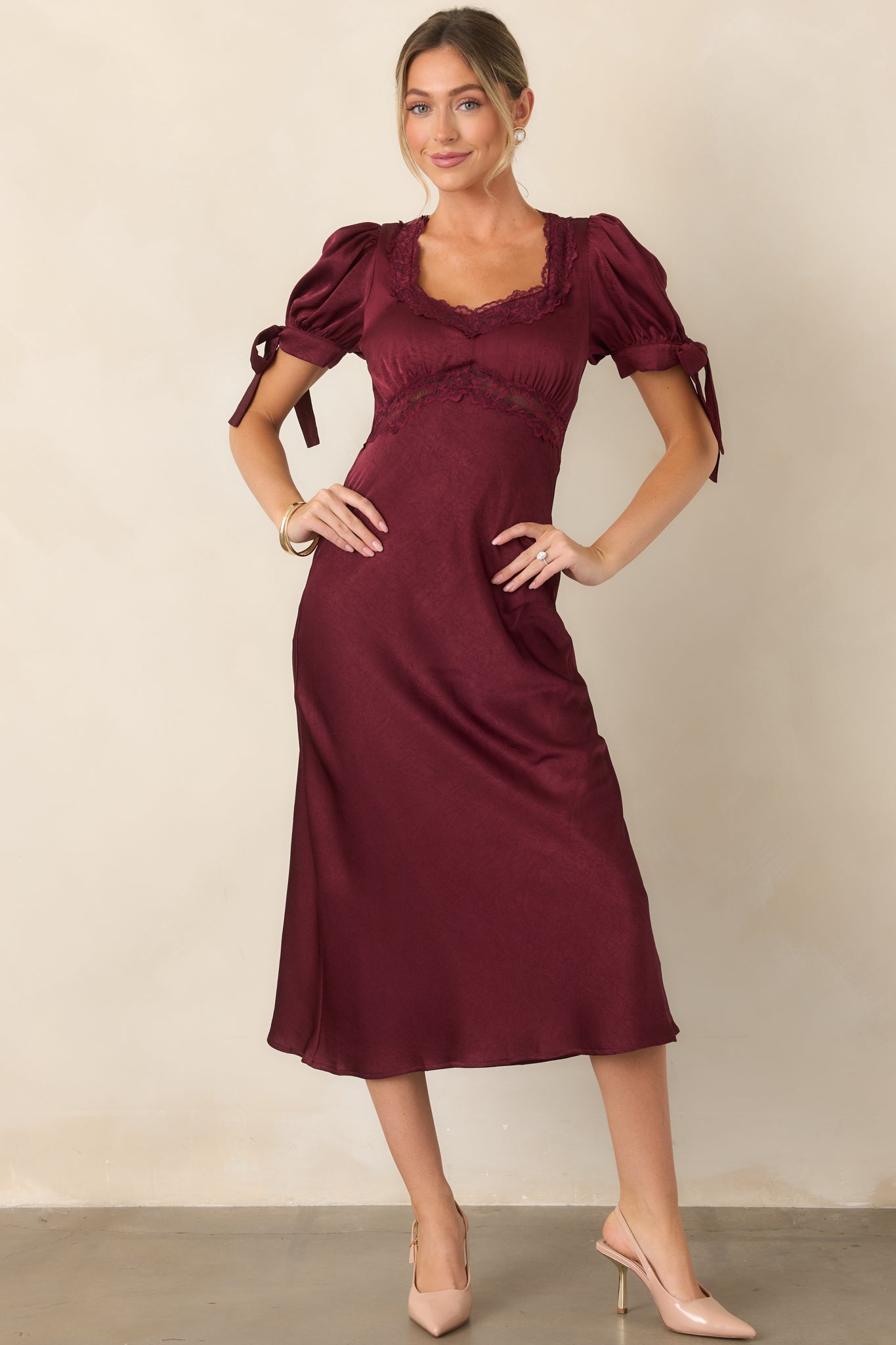 Lustrous satin dress showcasing its feminine puff sleeves, delicate lace accents, empire waist, and fluid midi-length skirt.