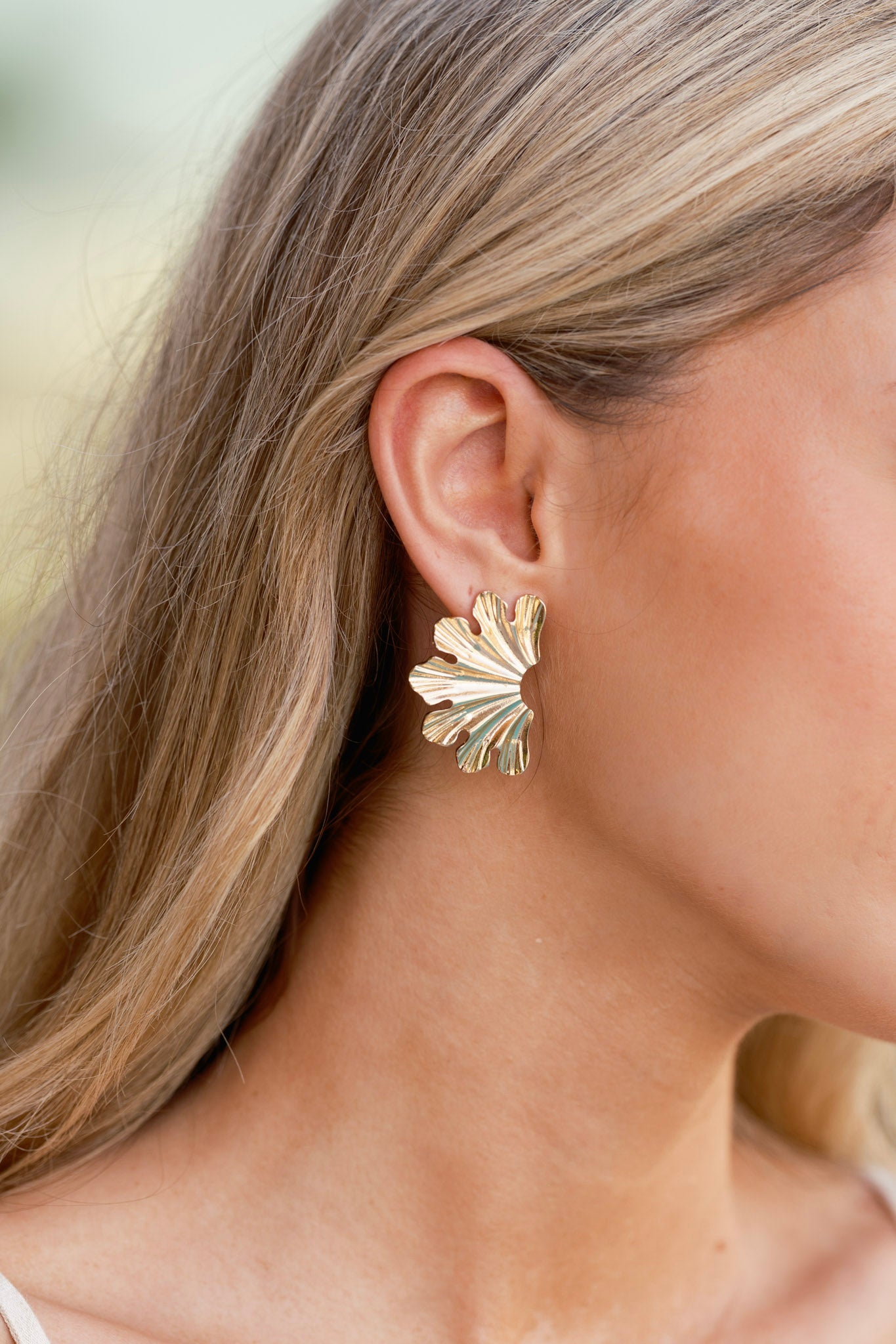 Macro detail of the earring’s textured gold finish and scalloped edge, with the post backing slightly visible in the background.