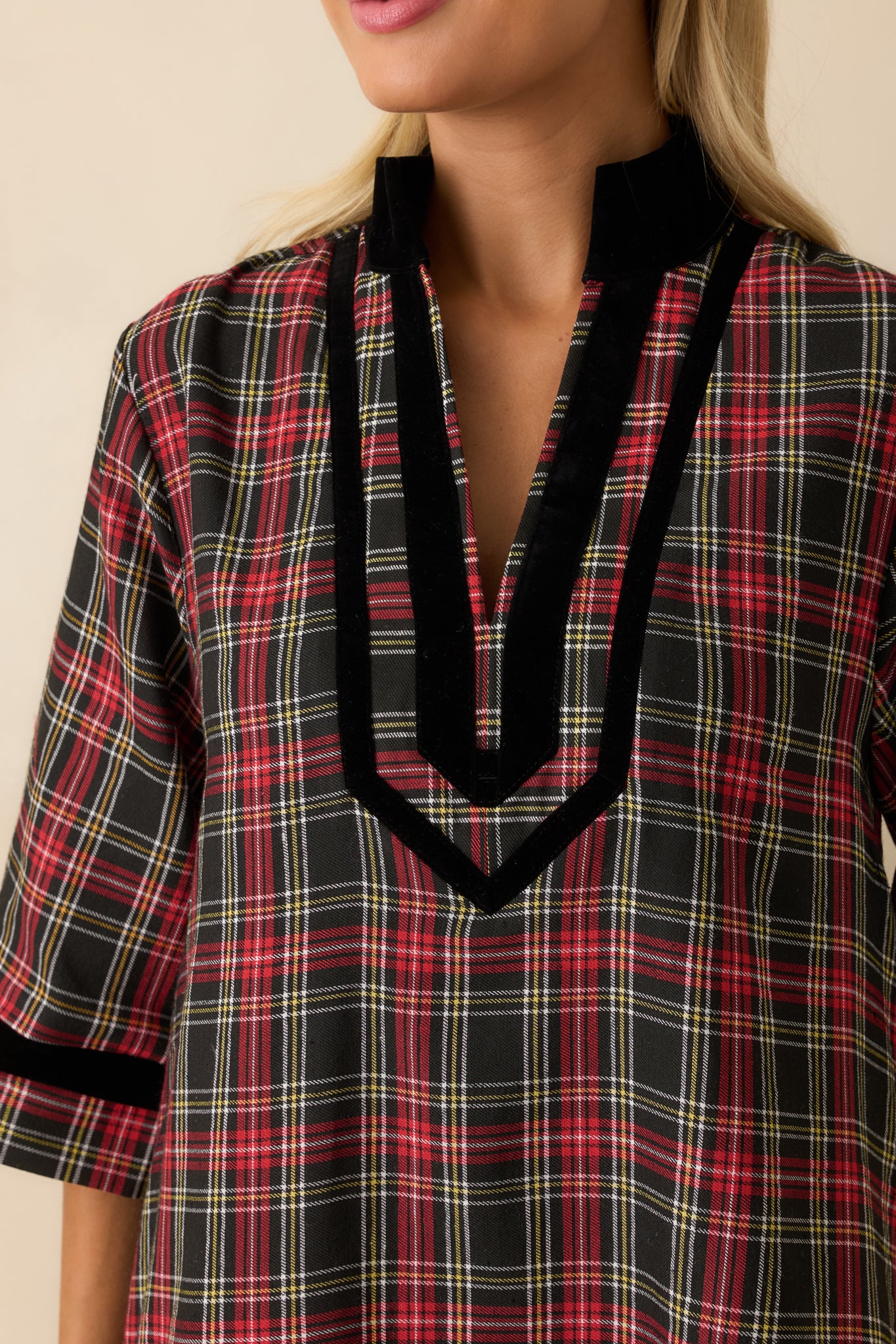 Macro view of plaid fabric, black velvet trim, and split neckline detailing on the red and black mini dress.