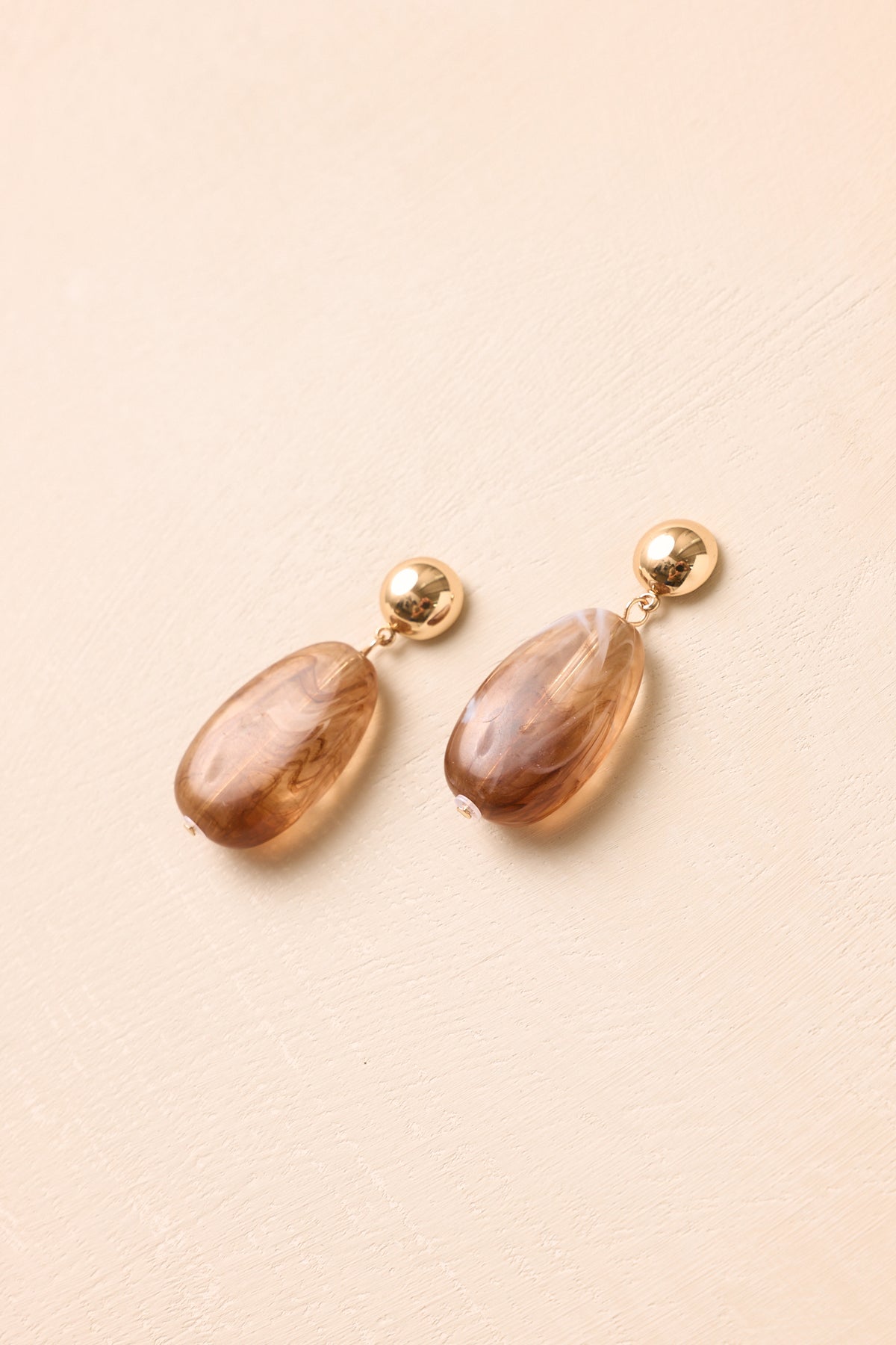 Marbled tortoise earrings showcasing polished gold-tone studs, organic color variations, and a graceful elongated oval design.
