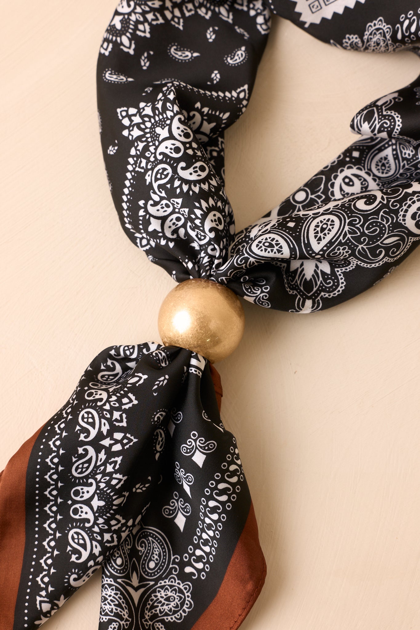 Matte gold scarf ring against a beige background showcasing its rounded silhouette, polished simplicity, and versatile modern design.
