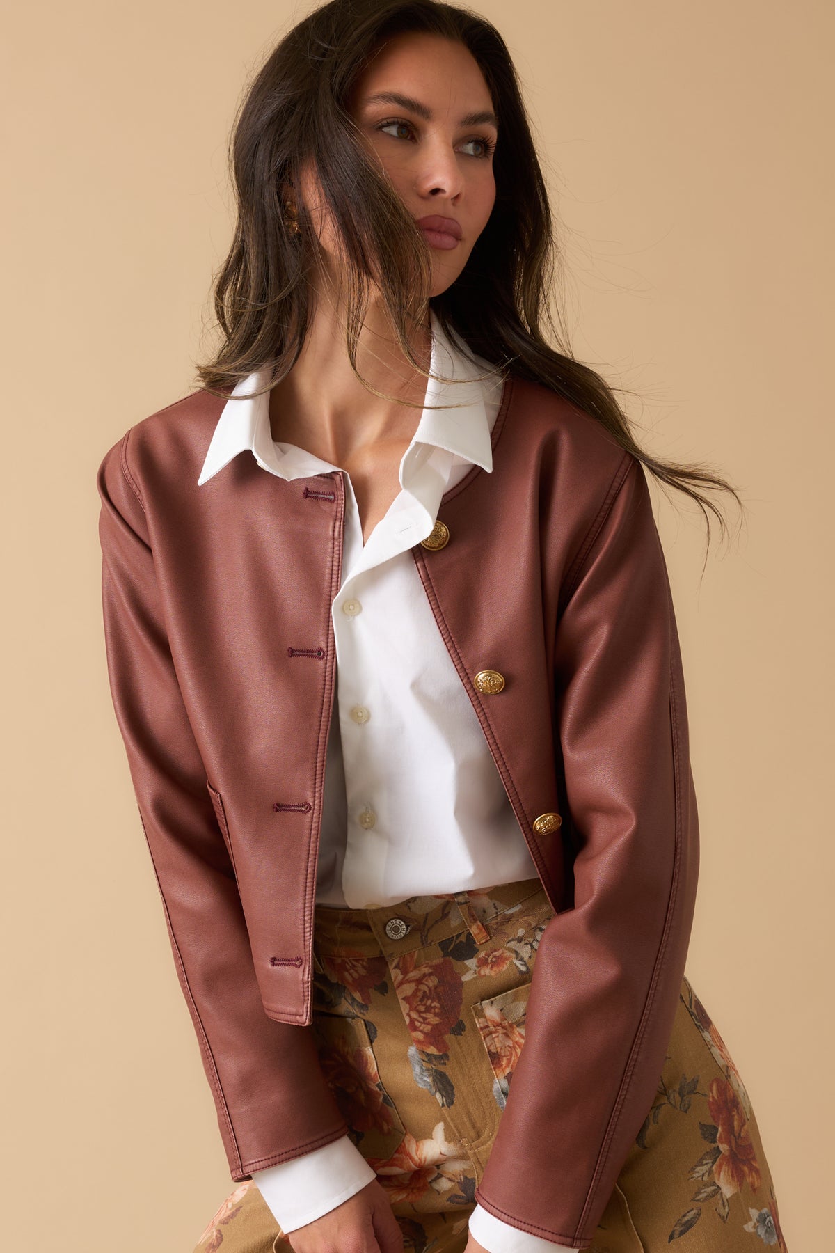 Mauve faux leather cropped jacket featuring a round neckline, embossed gold buttons, structured seams, and front welt pockets.