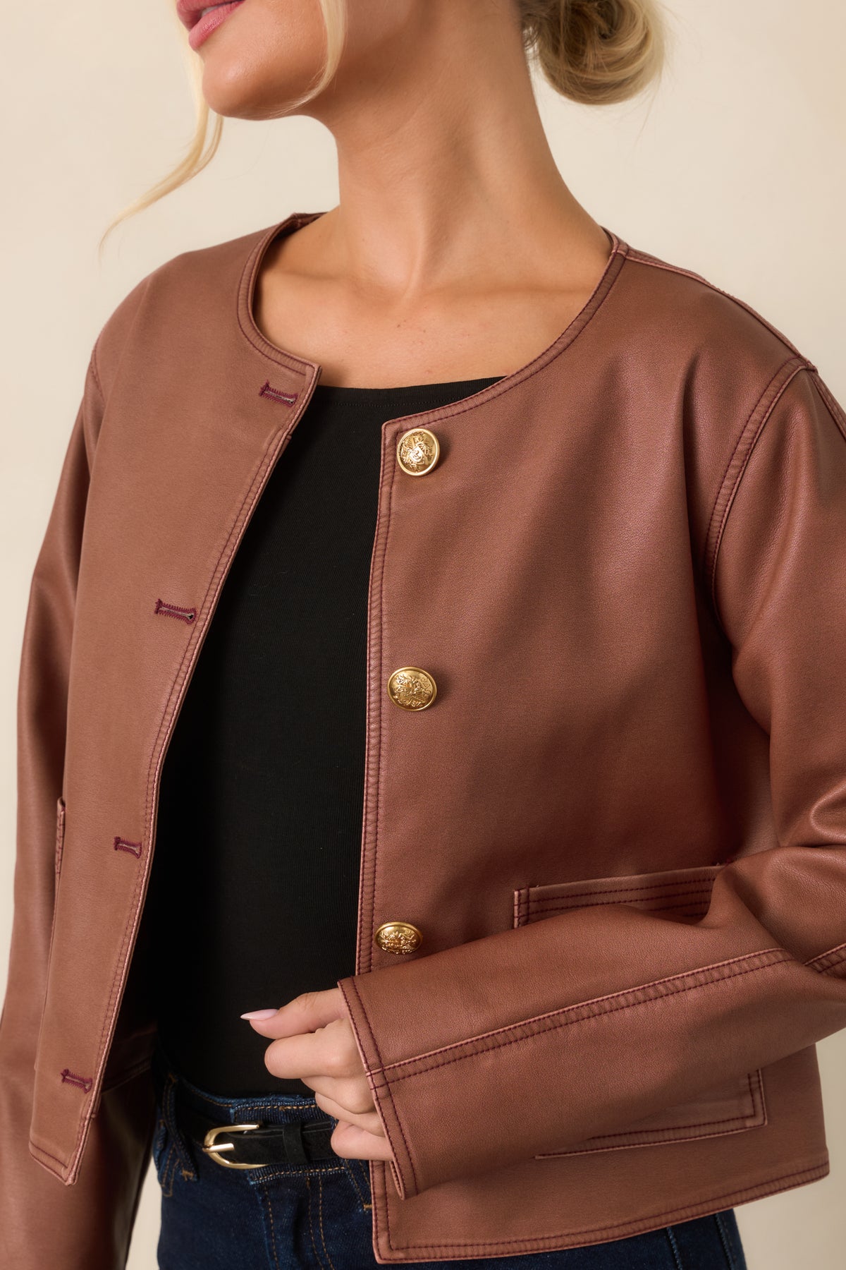 Close detail of the mauve faux leather, embossed gold button, and structured seam detailing.