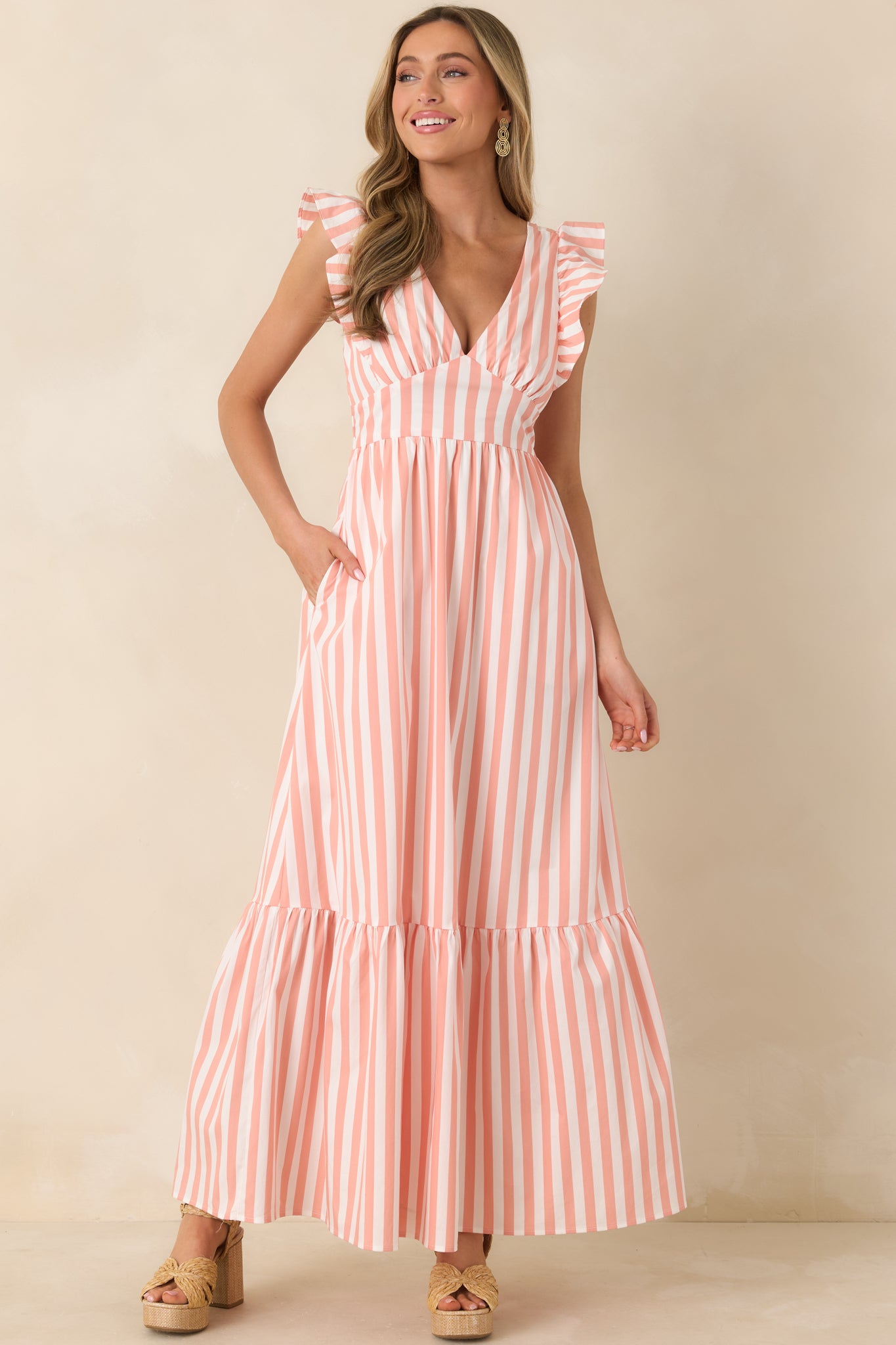 Elegant maxi with plunging neckline, structured flutter straps, fitted bodice, and cascading tiered skirt for a breezy, summery silhouette.