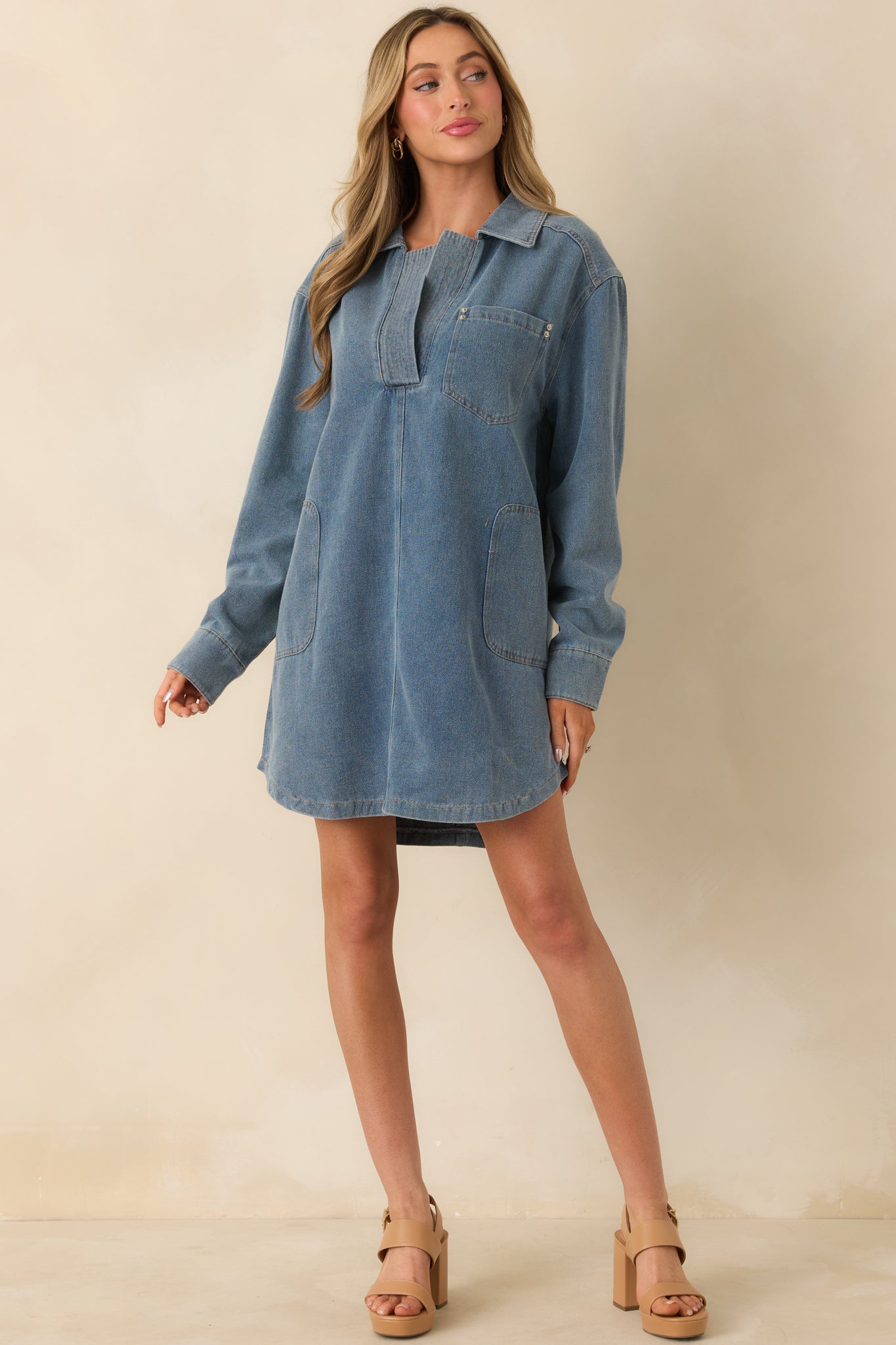 Angled front view of the medium denim mini dress highlighting the relaxed fit, front patch pockets, and straight hemline.