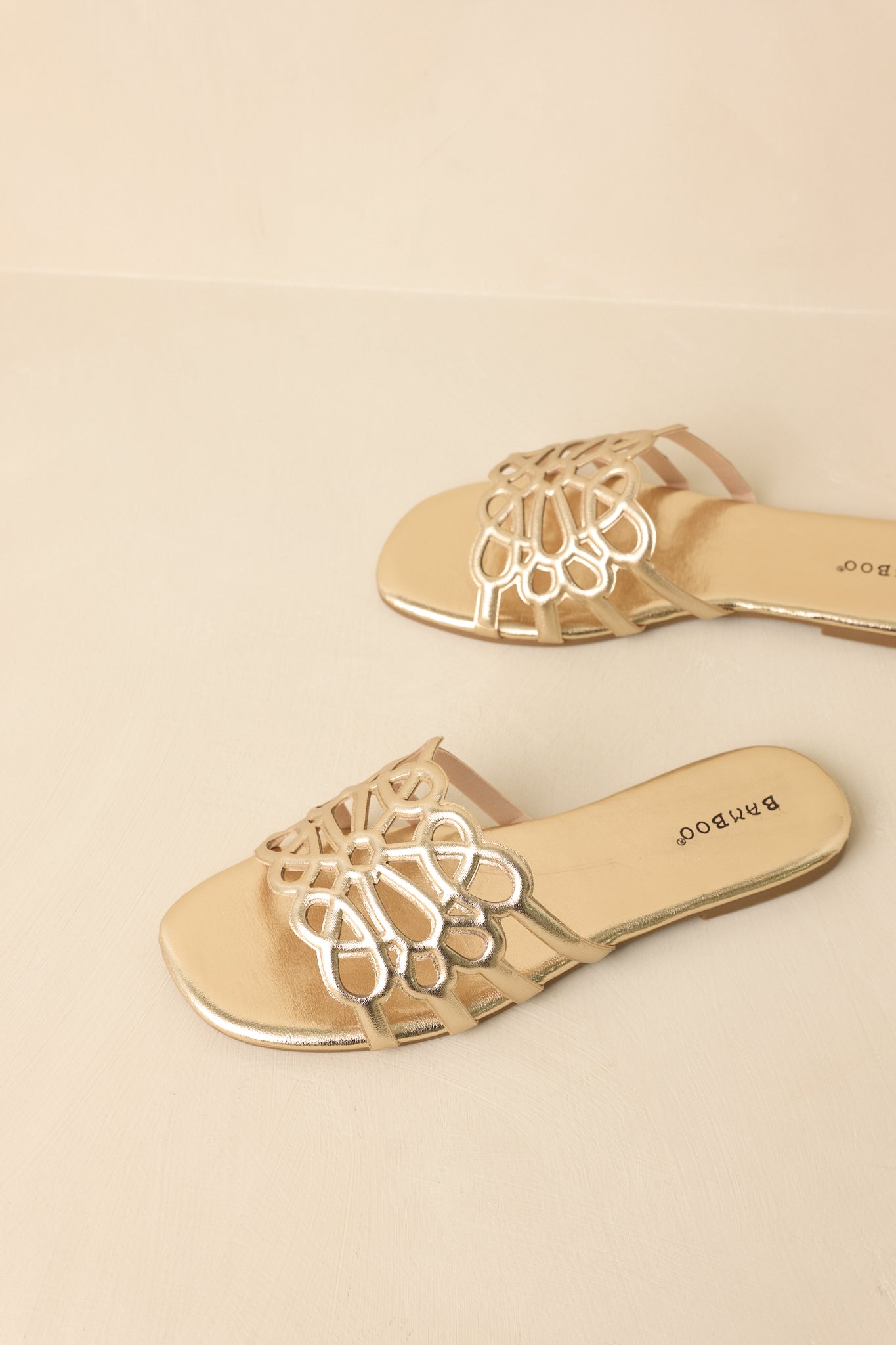 Metallic gold slide sandals displayed on a beige background, showcasing open-toe design and wide strap
