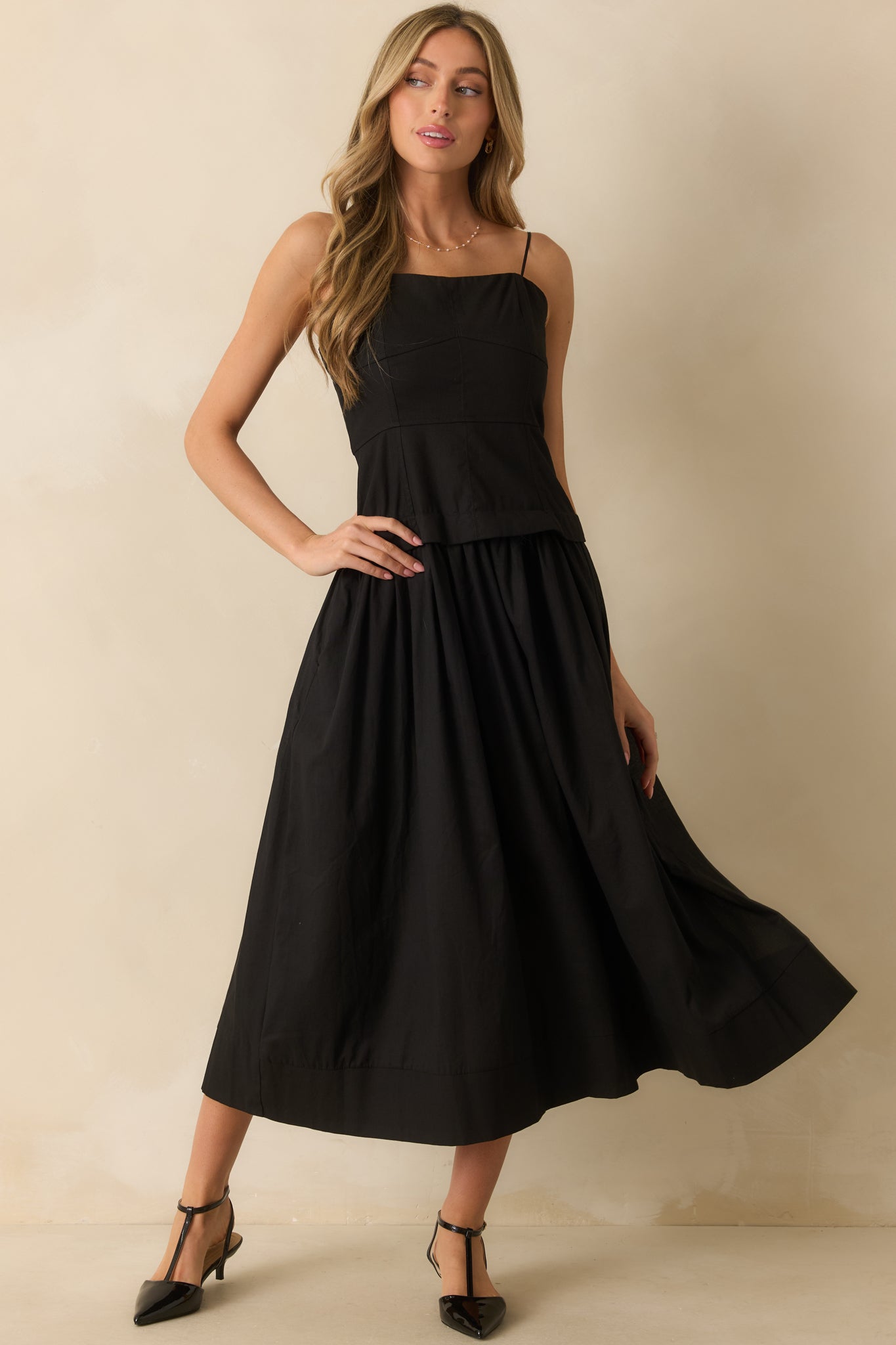 Midi-length black dress with functional pockets, concealed back zipper, and a feminine paneled bodice.