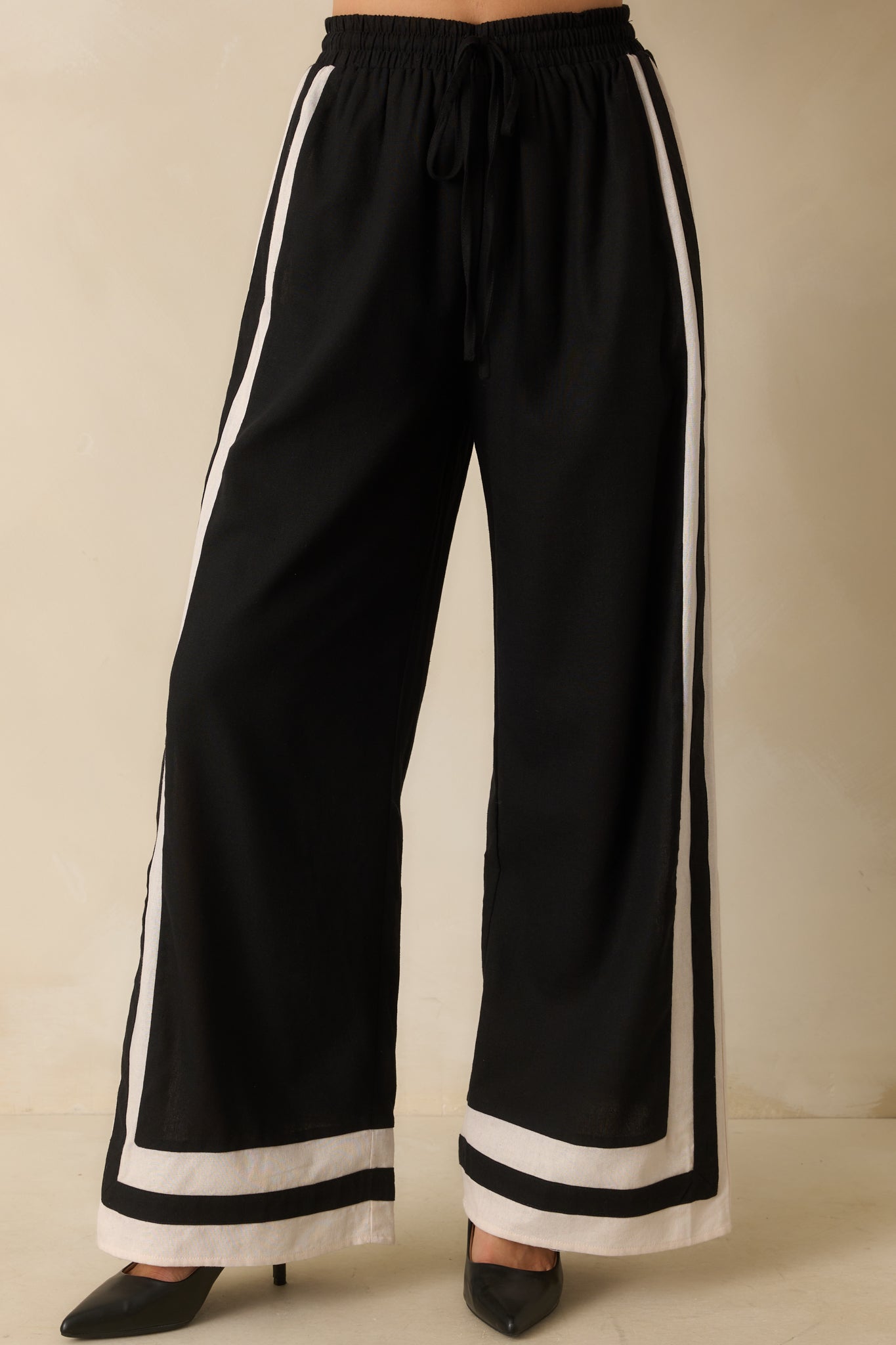 Midsection view highlighting the elastic waistband, adjustable drawstring, and contrast trim of black wide-leg pants.