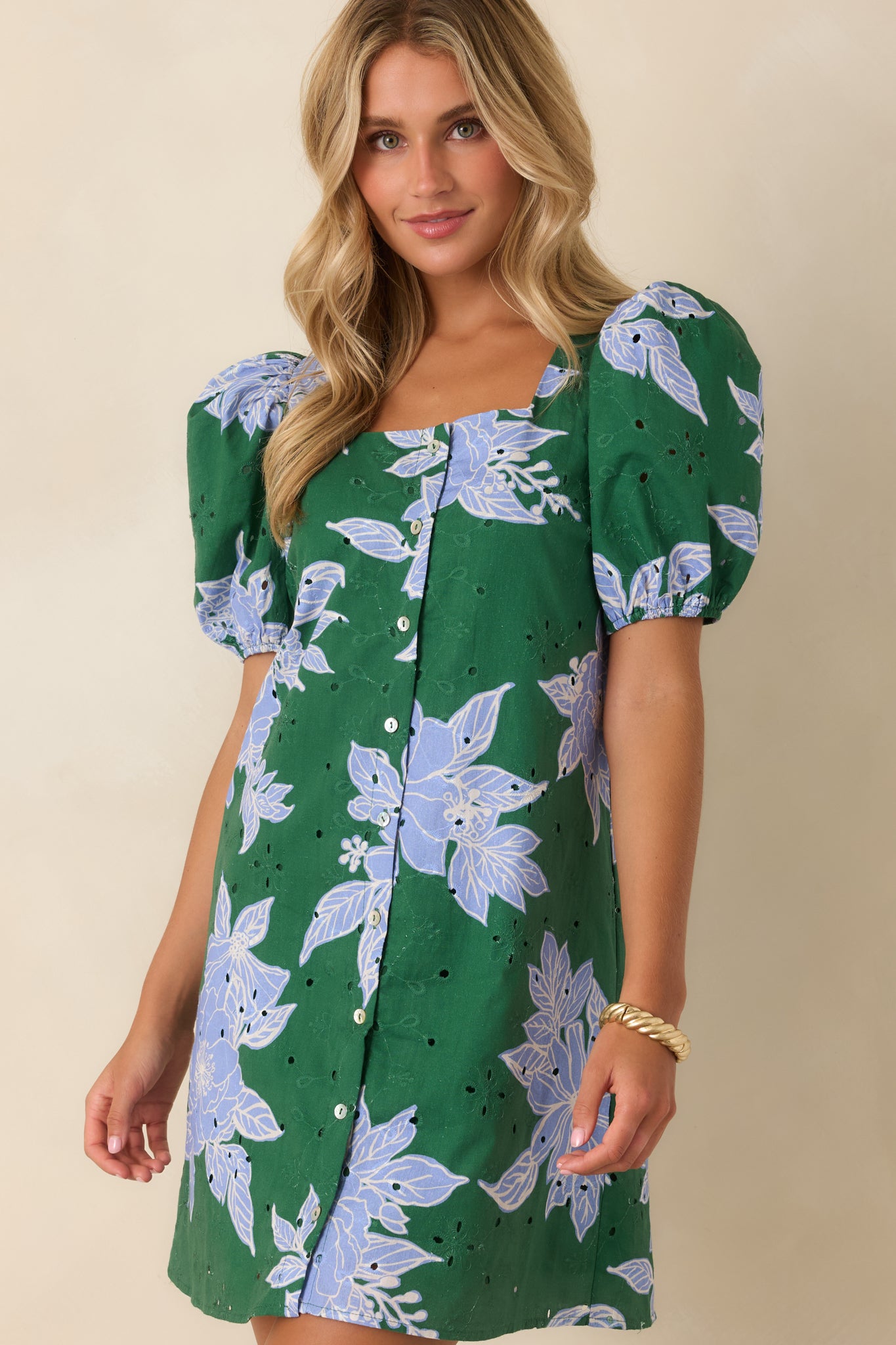 Mini shift dress featuring vibrant green fabric, oversized blue flowers, textured eyelet embroidery, and puff sleeves.