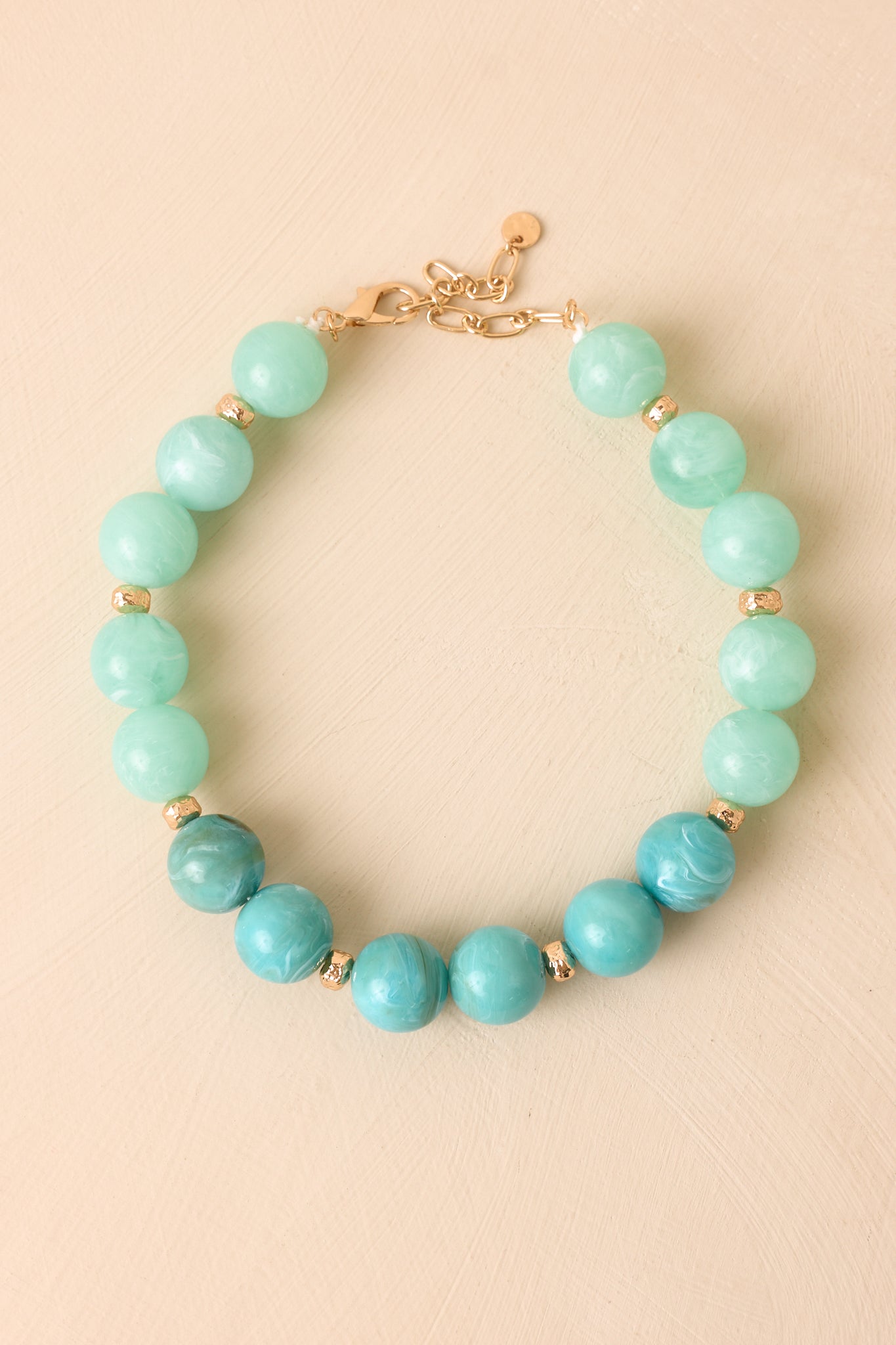 Oversized marbled bead necklace displayed with mint and blue tones and polished gold-tone spacers.