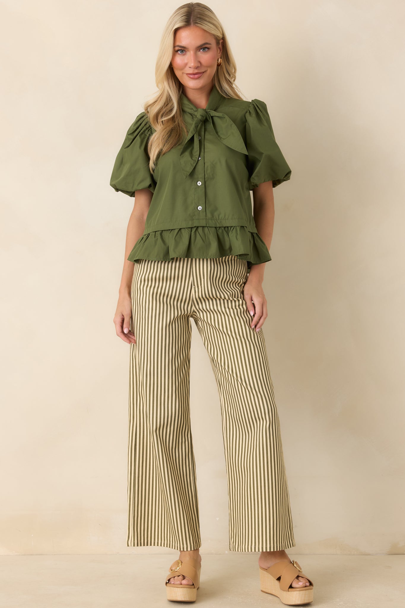 Moss green blouse featuring a statement bow tie neckline, voluminous puff sleeves, and a flounced peplum hem for a feminine silhouette.