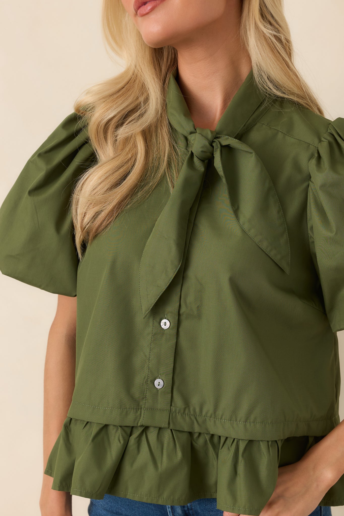 Close-up of the moss green blouse featuring the statement bow tie neckline, gathered details, and refined finish.