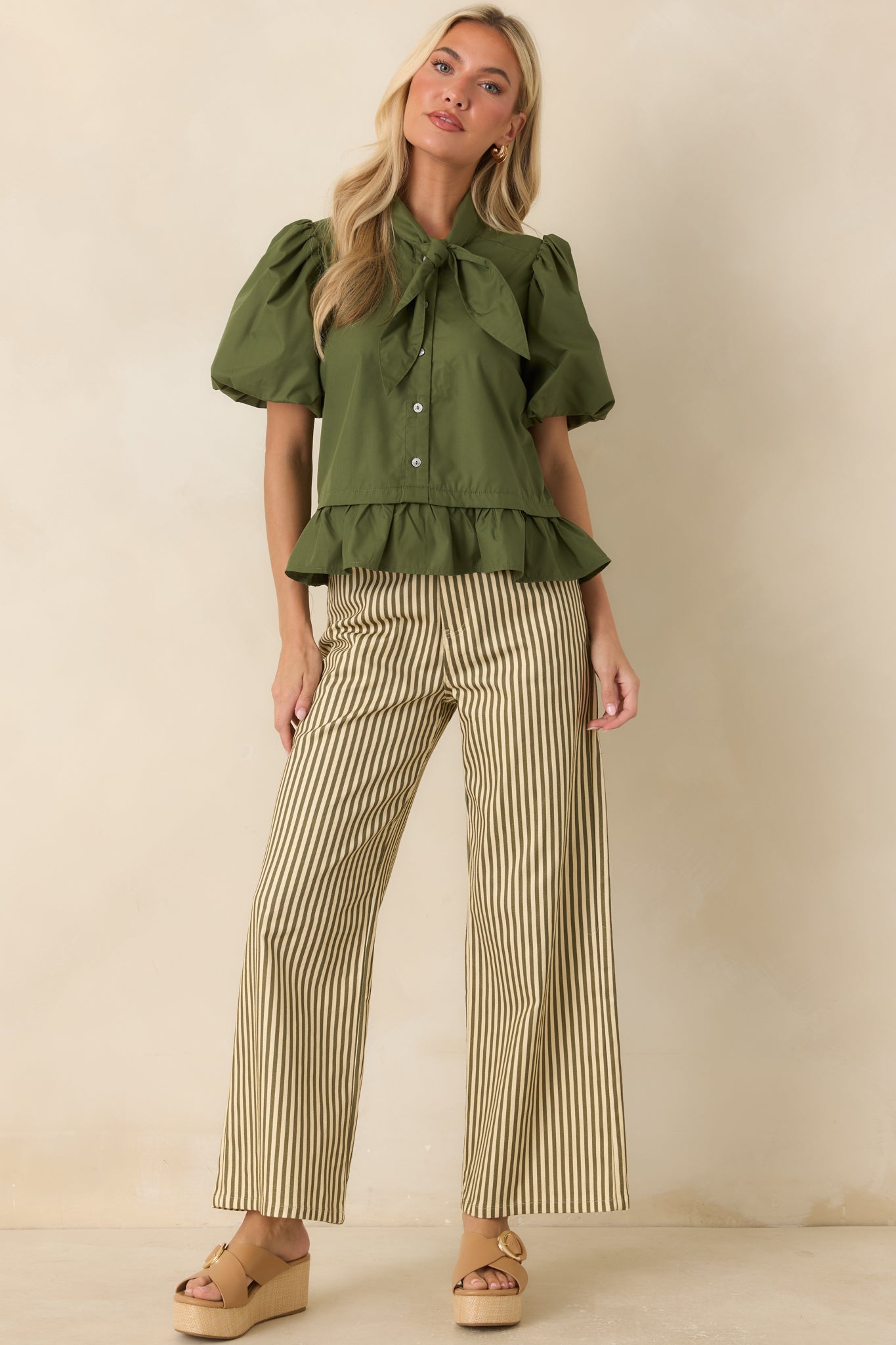 Rich moss green top showcasing dramatic puff sleeves, a polished bow neckline, and a softly flared peplum hem.