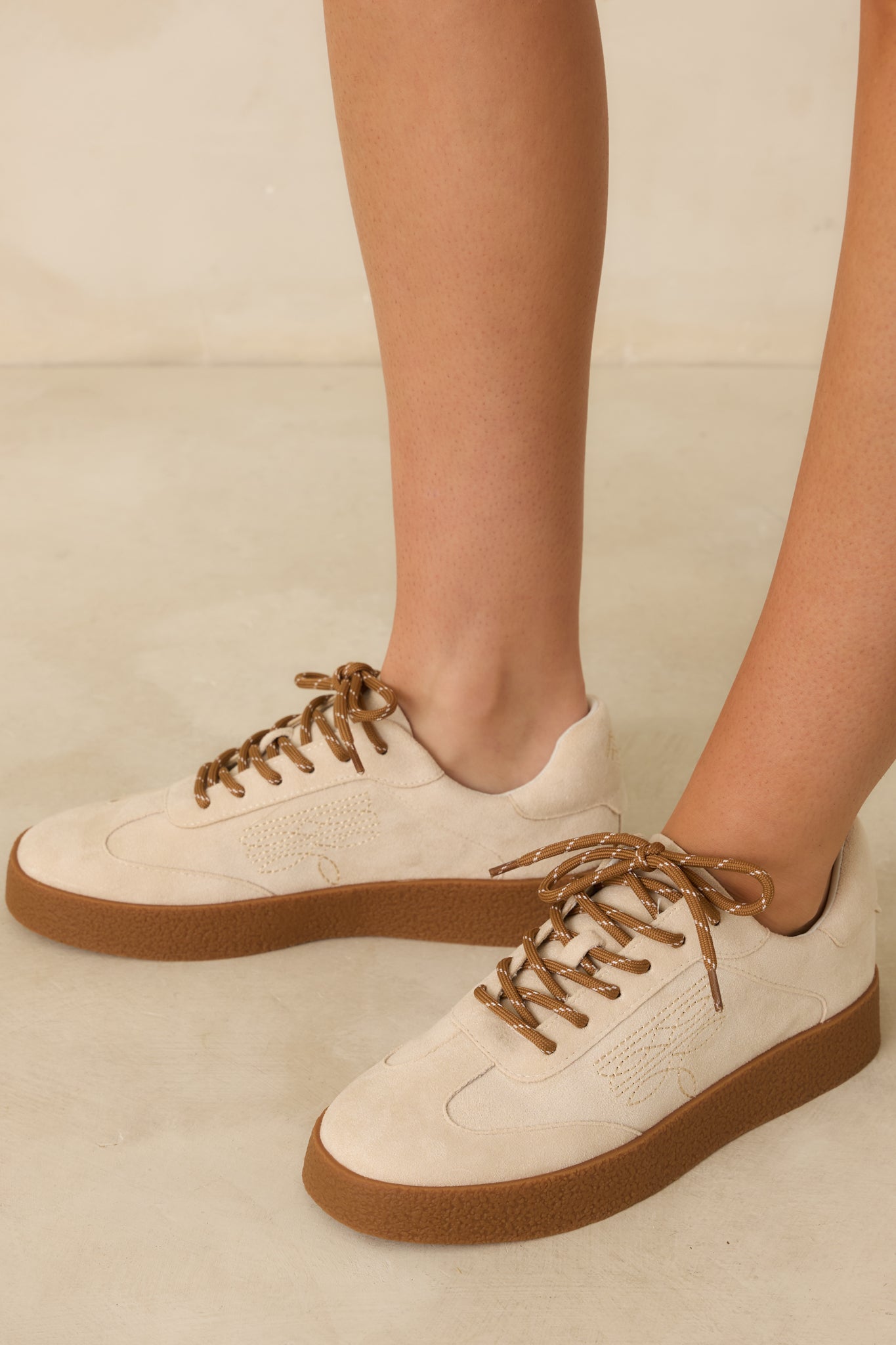 Front-facing view of natural faux suede sneakers showing rounded toe and lace-up design.