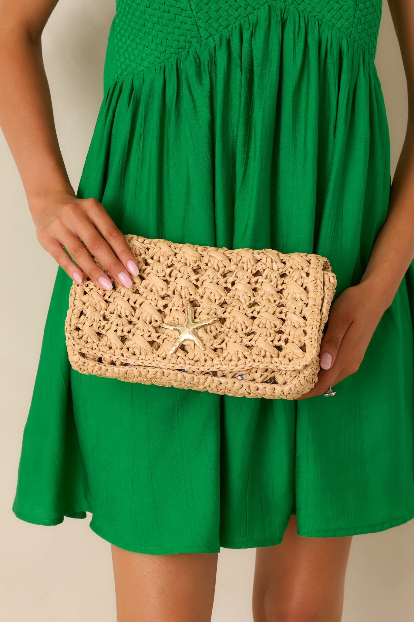 Natural raffia clutch featuring an open woven design, structured silhouette, gold starfish accent, and removable chain strap.
