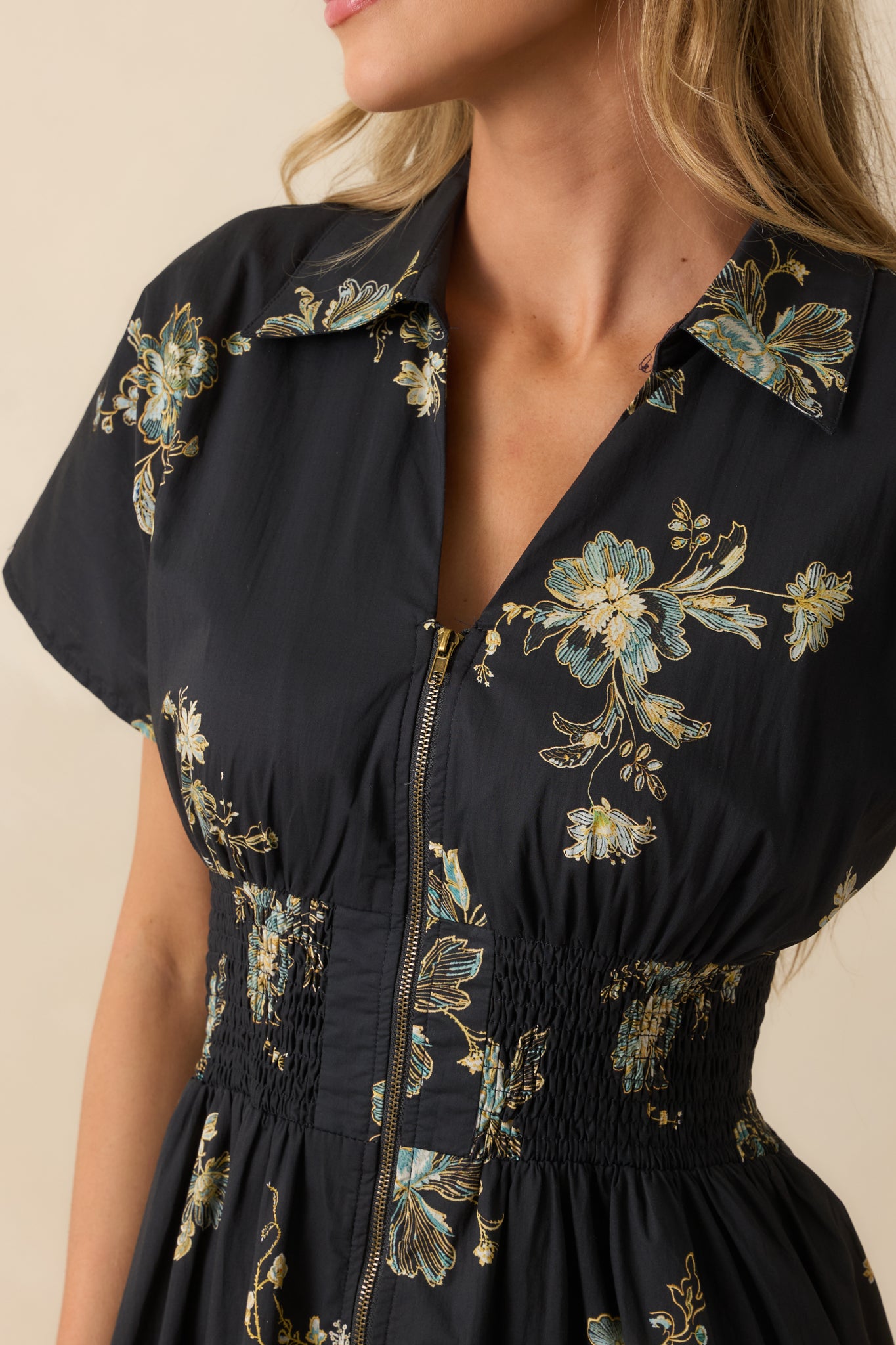 A close-up detail of the navy dress showing a collared v-neckline, smocked waistband, and floral print texture.