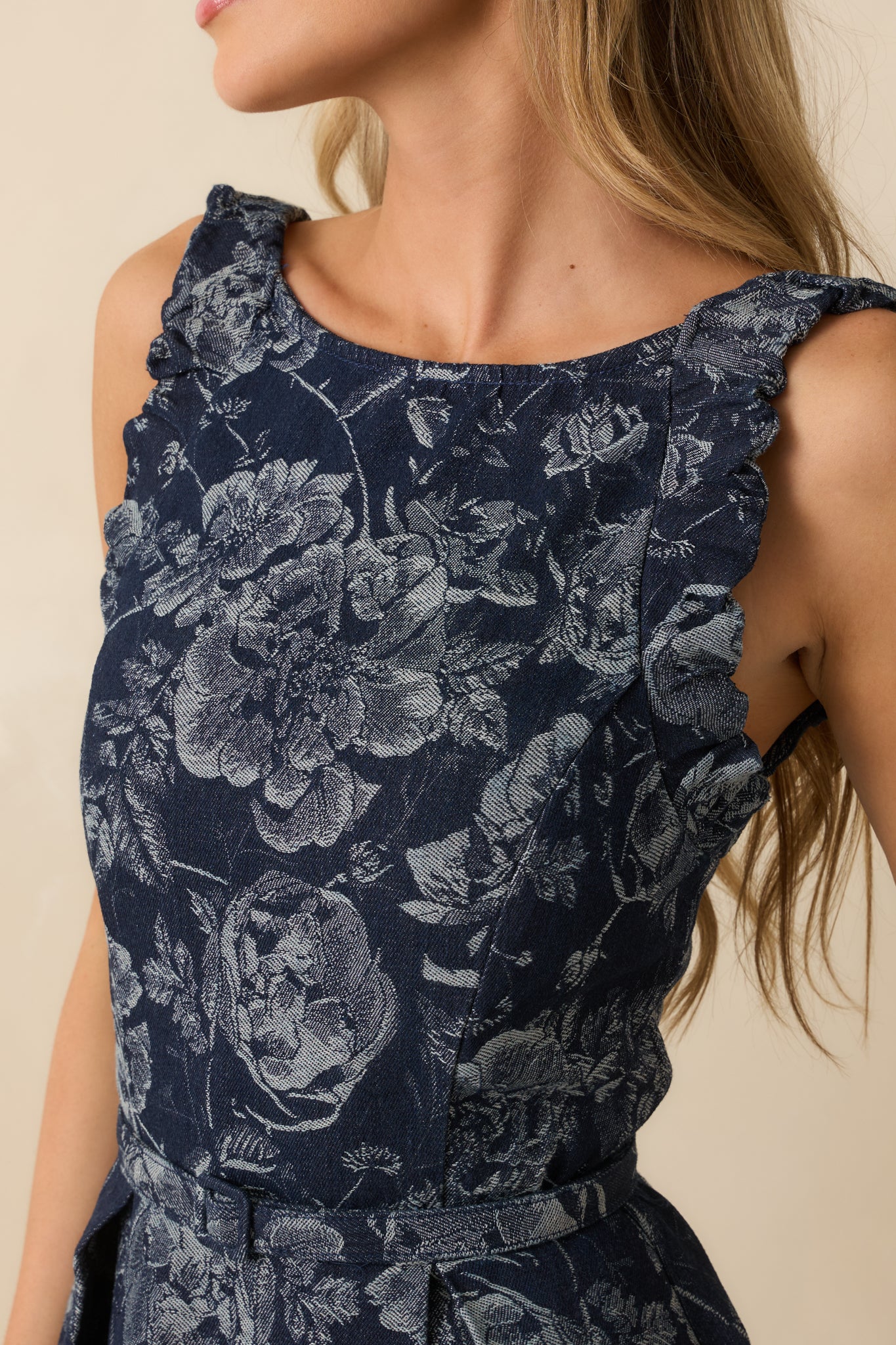 A close-up detail of the navy dress showing floral jacquard fabric texture, ruffle-trim straps, and pleated skirt detail.