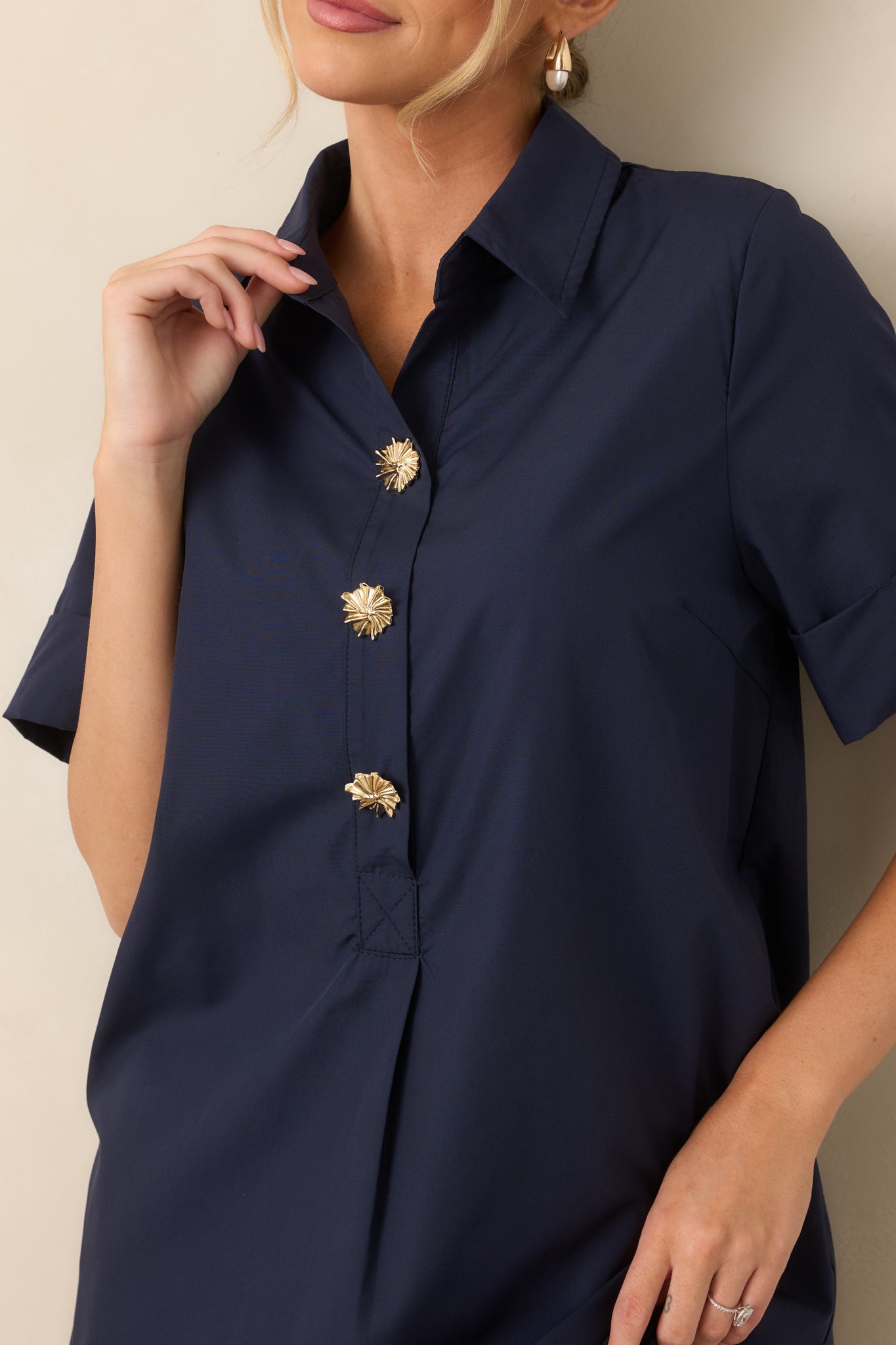 Close-up of the navy woven fabric, collared neckline, and statement gold floral buttons along the front placket.