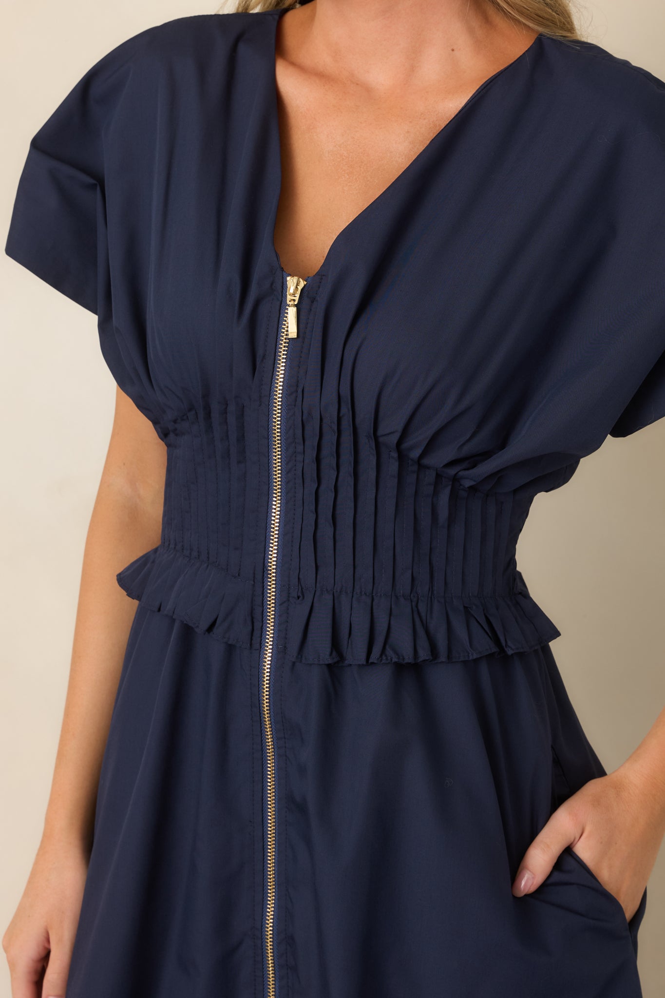 Close-up of the V-neckline, front zip closure, and wide smocked waistband with delicate ruffled trim.