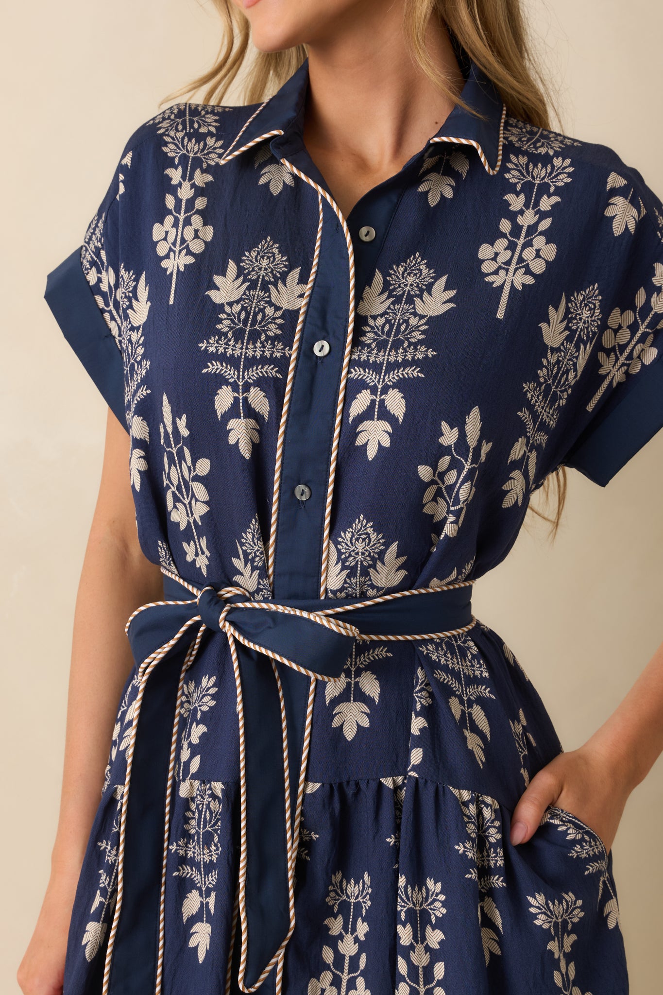 Up-close of the navy fabric showing ivory floral print, stripe contrast piping, and button front closure.