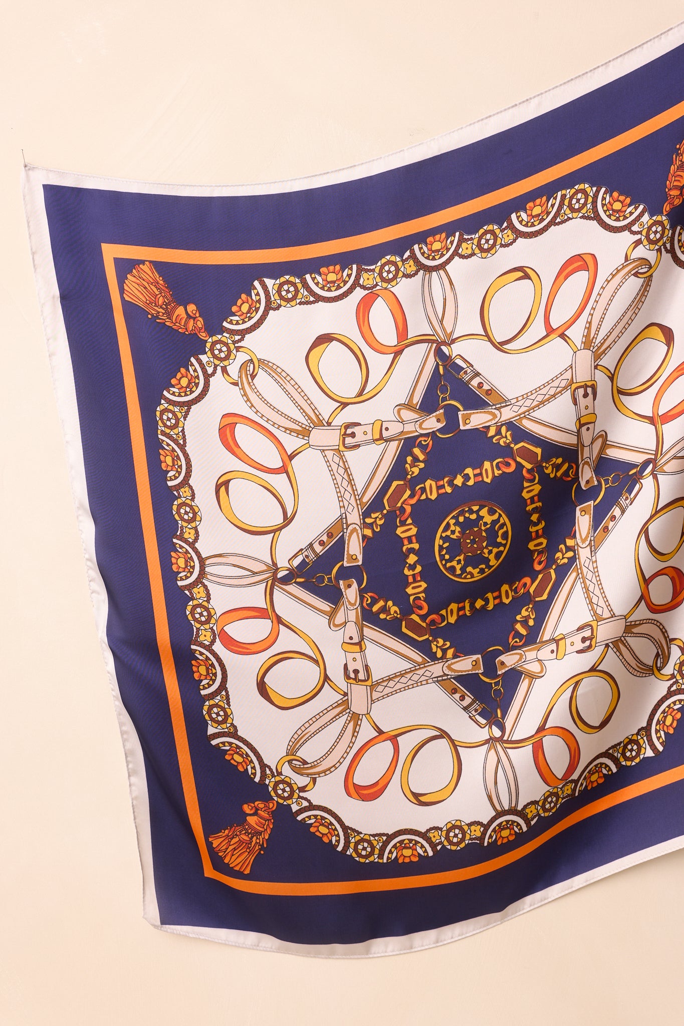 Full view of the navy hair scarf featuring a multicolor chain, belt, and tassel motif with a gold and orange border on satin woven fabric.