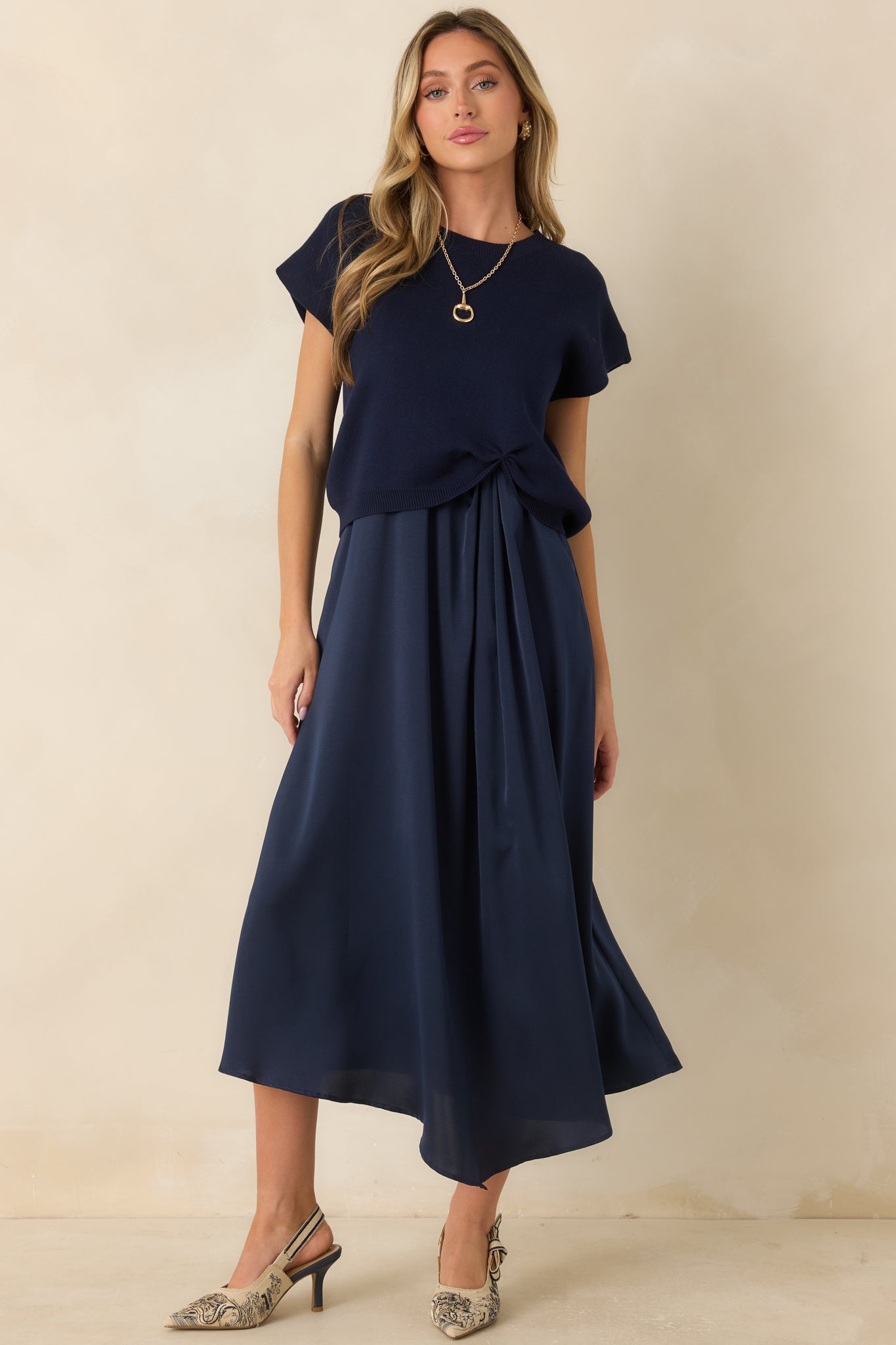 Navy knit sweater featuring a relaxed silhouette, cap sleeves, ribbed neckline, and a cinched front hem detail.