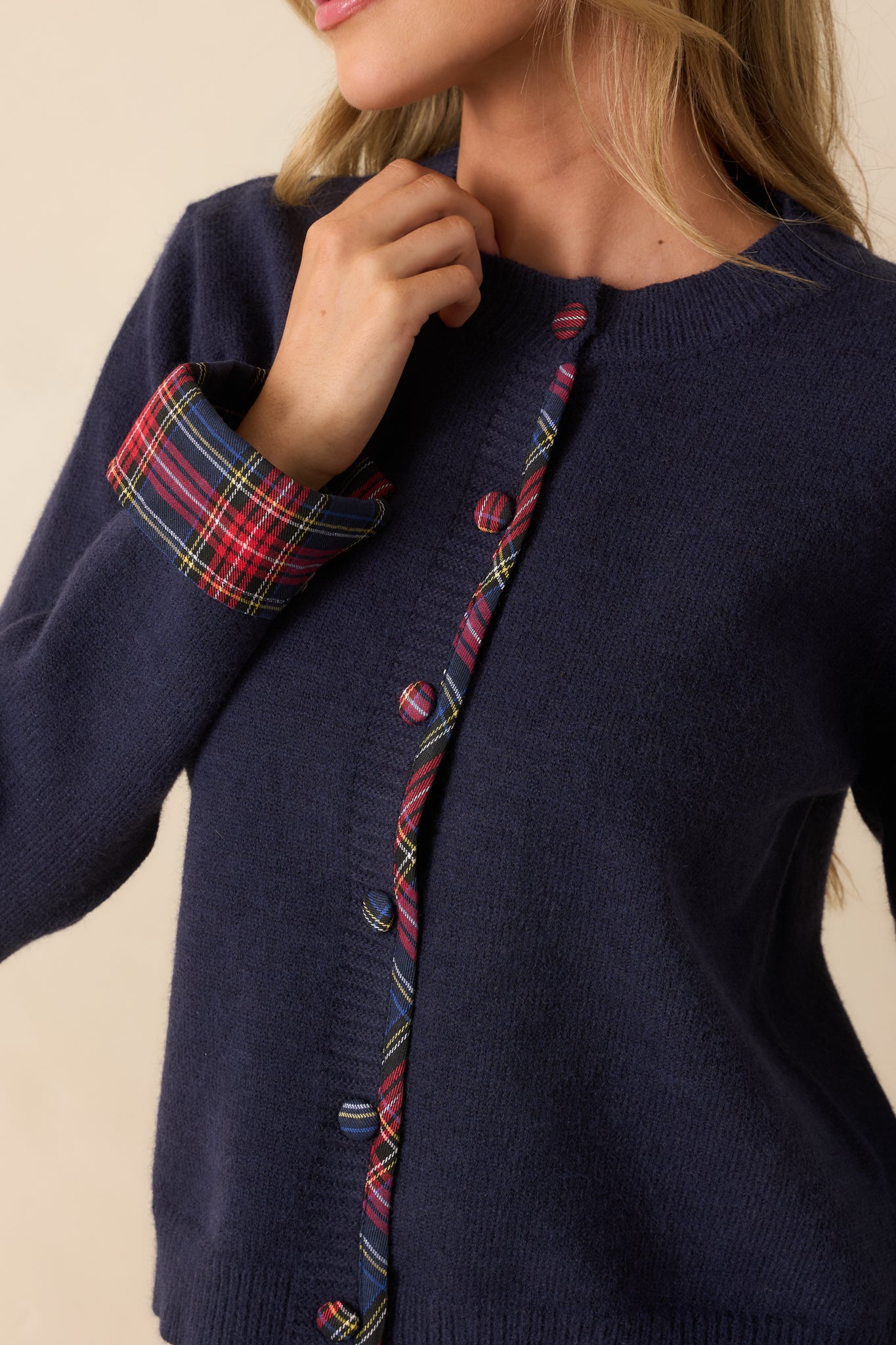 Tight detail showing the navy knit texture with covered plaid buttons and tartan placket trim.